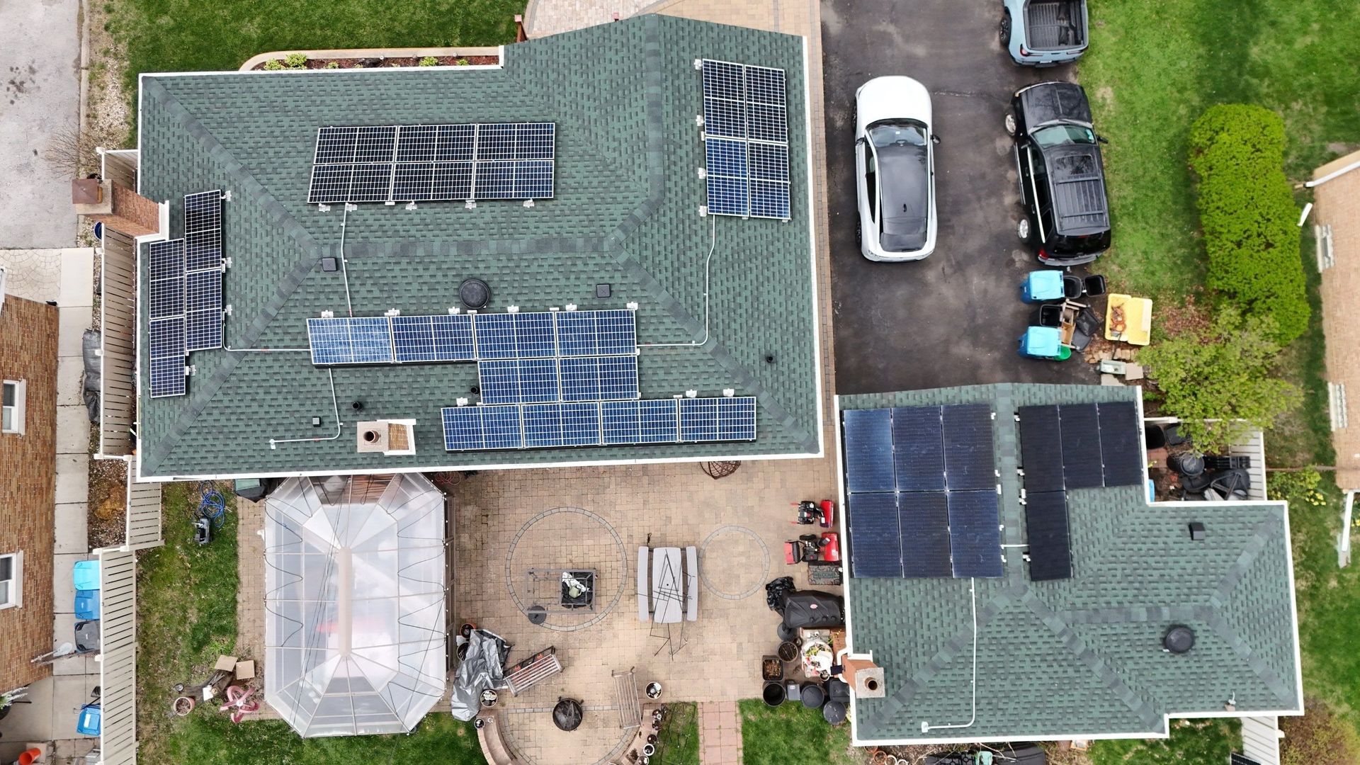 Overhead view: houses with solar panels on green roofs, parked cars, and a backyard.