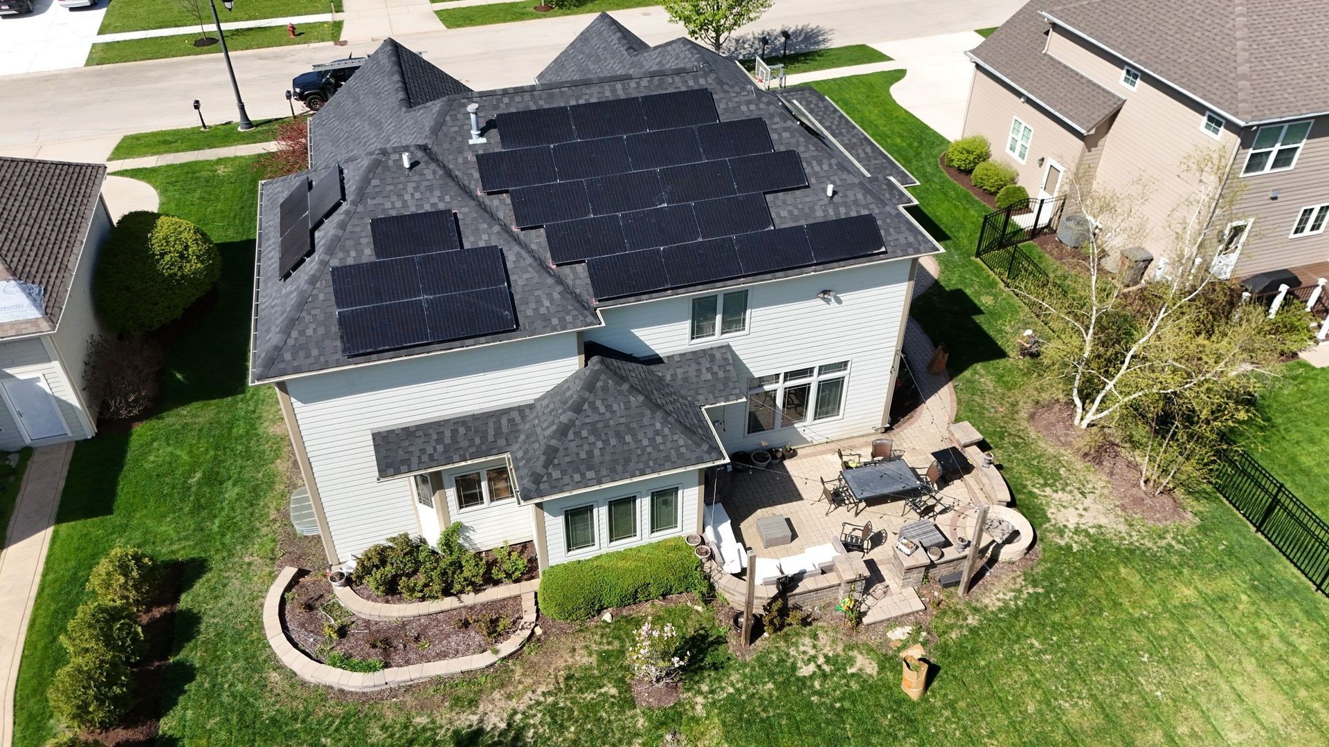 Overhead view of a two-story house with solar panels on the roof, in a suburban neighborhood.