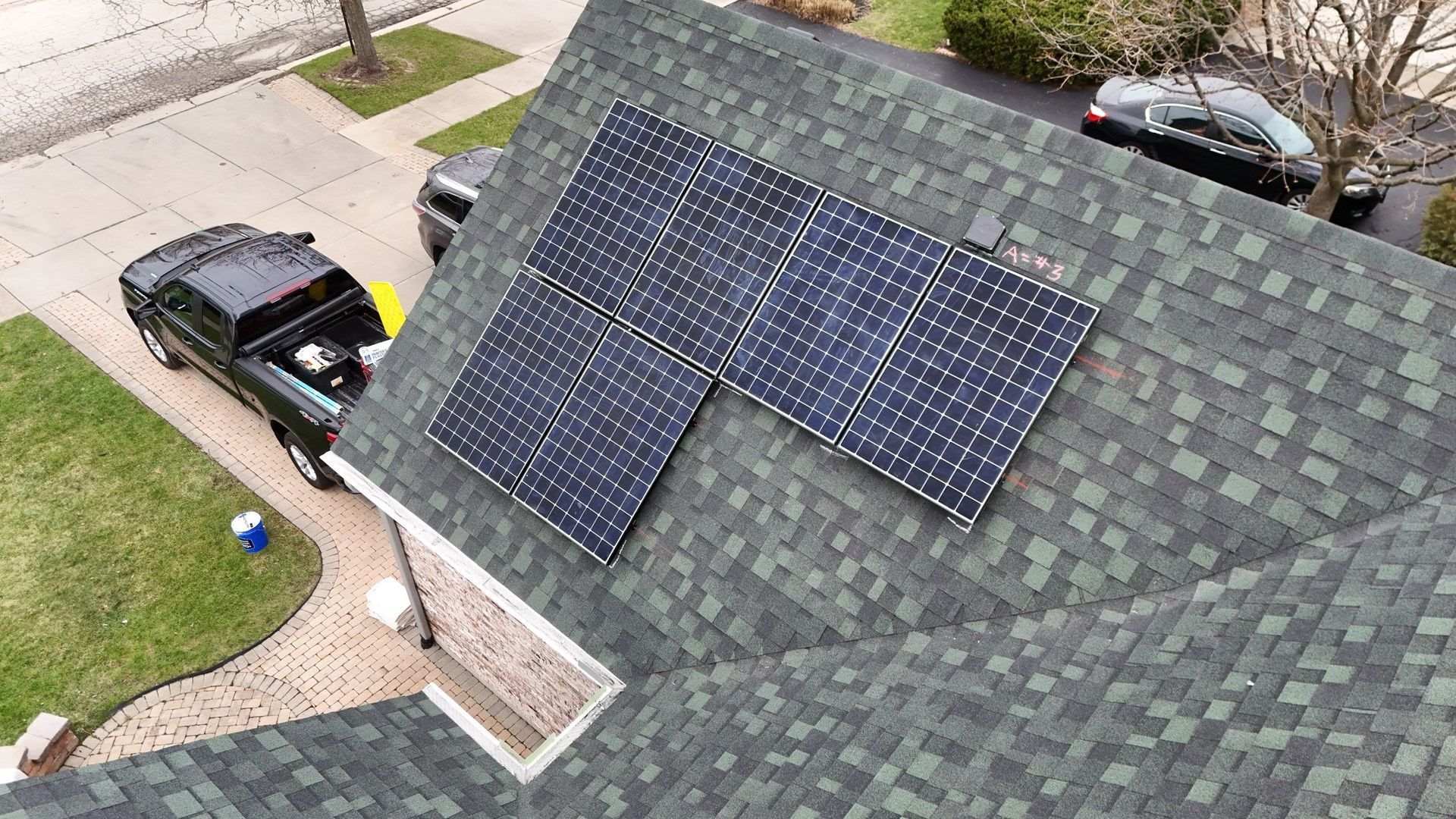 Solar panels installed on a green shingle roof. A black truck is parked in the driveway.