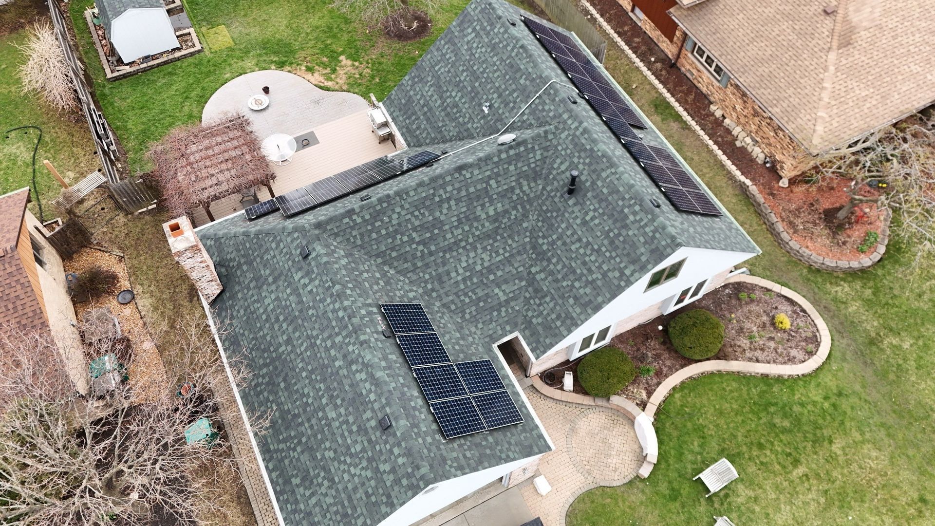 Aerial view of a house with solar panels on the roof, a patio, and surrounding lawn.