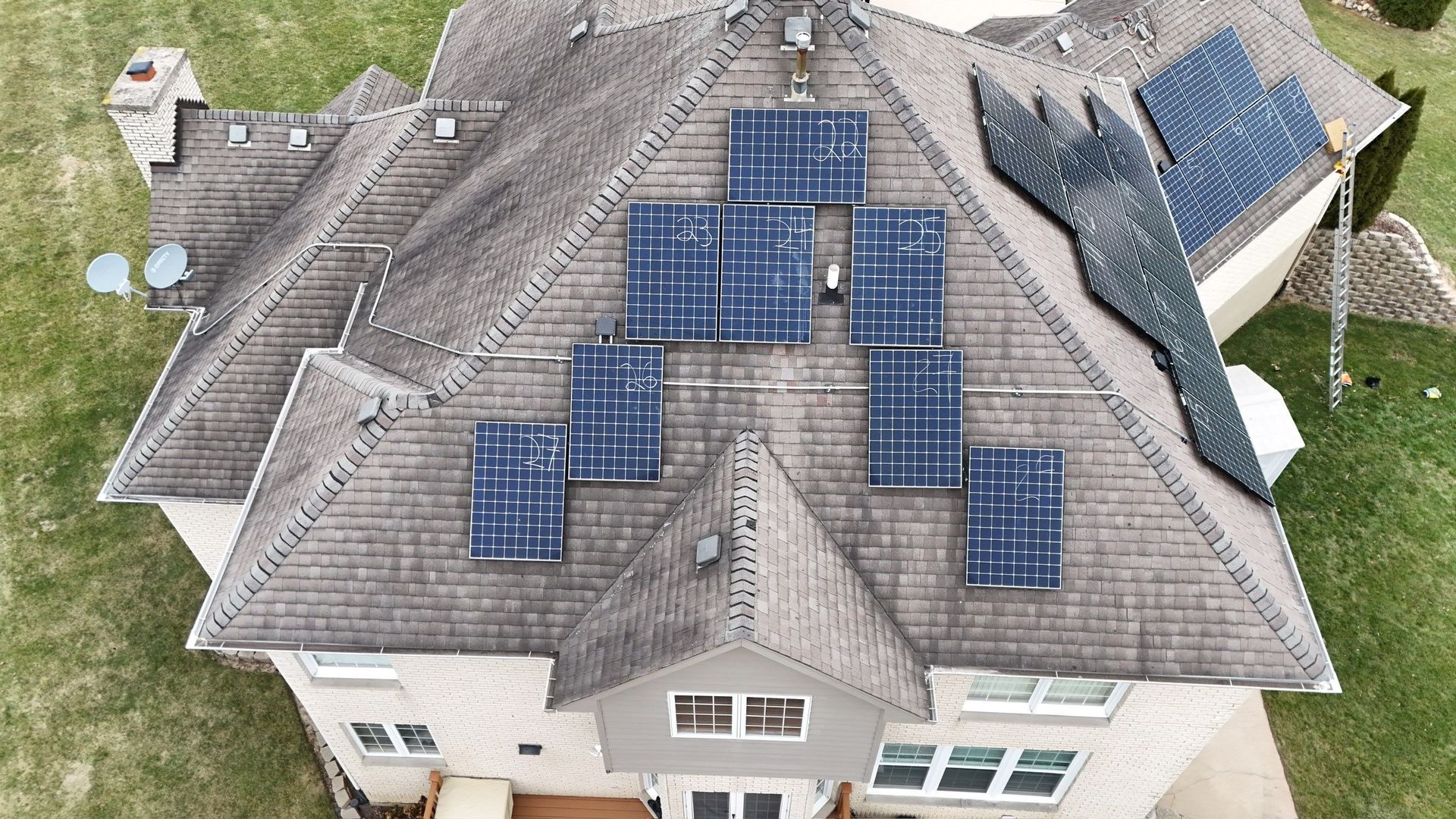 Overhead view of a house with solar panels installed on its roof, surrounded by green grass.