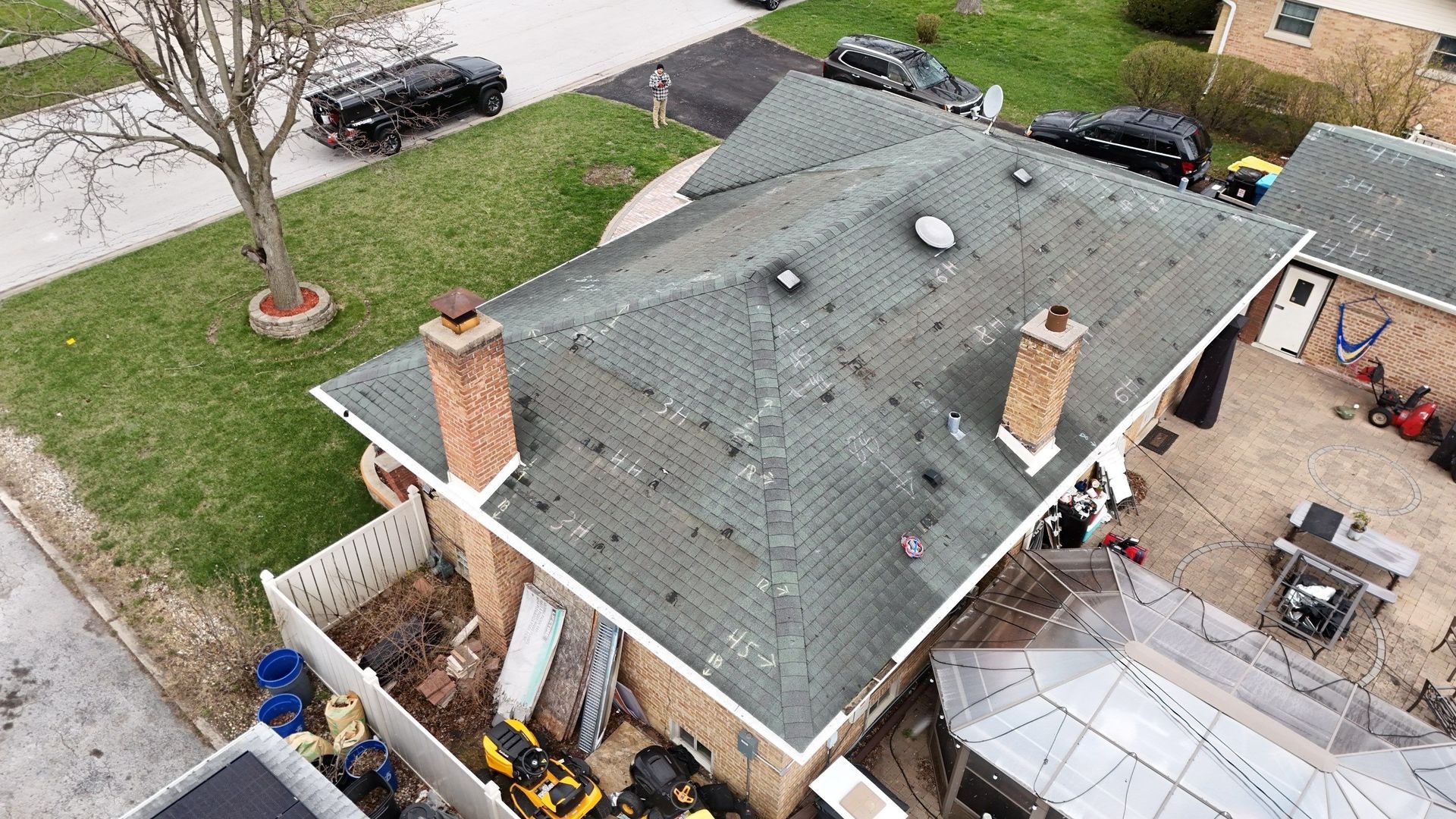 Overhead view of a brick house with a weathered green roof, chimney, and yard in a residential neighborhood.
