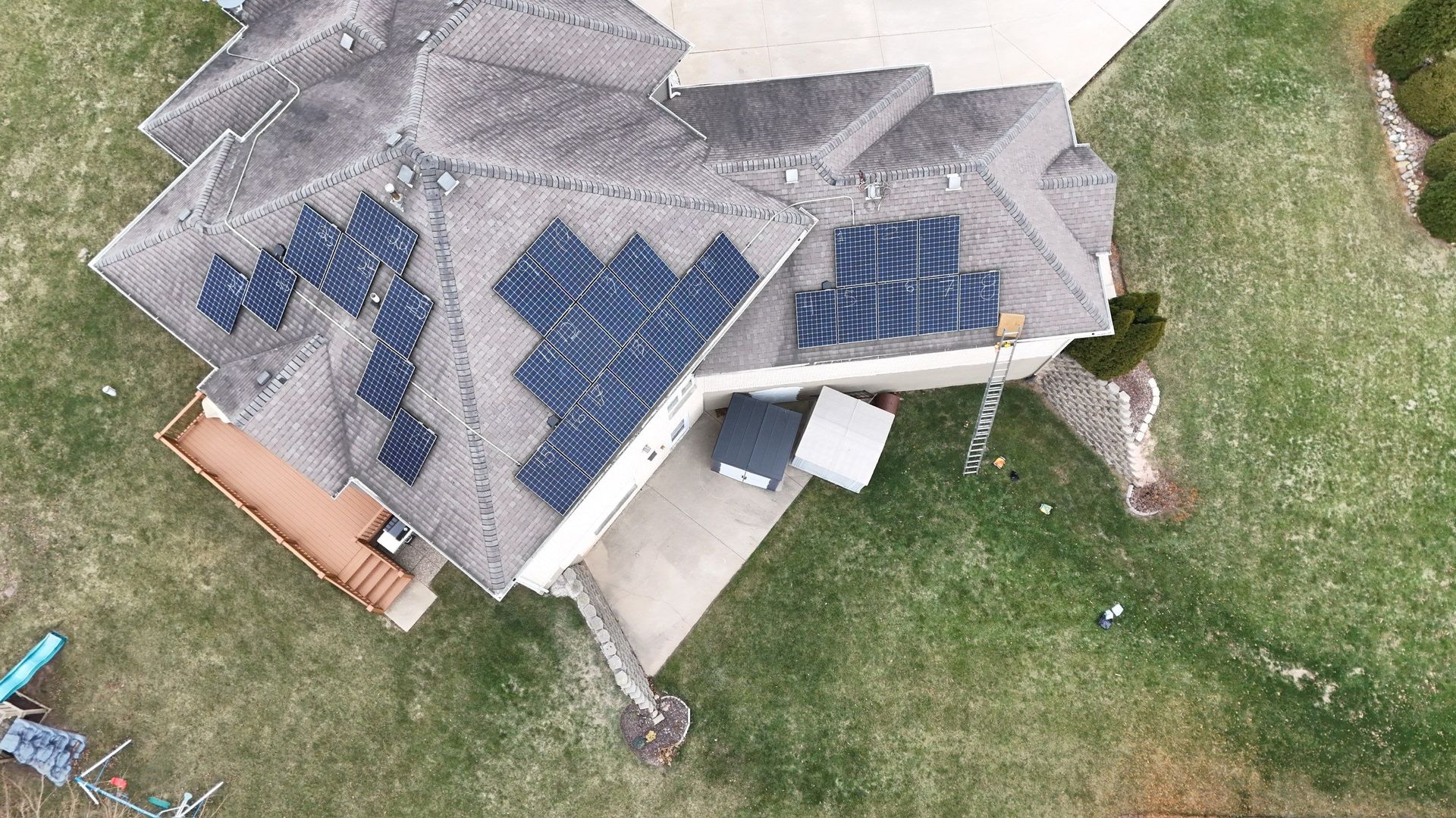 Overhead view of a house with solar panels on the roof, surrounded by green grass and a driveway.