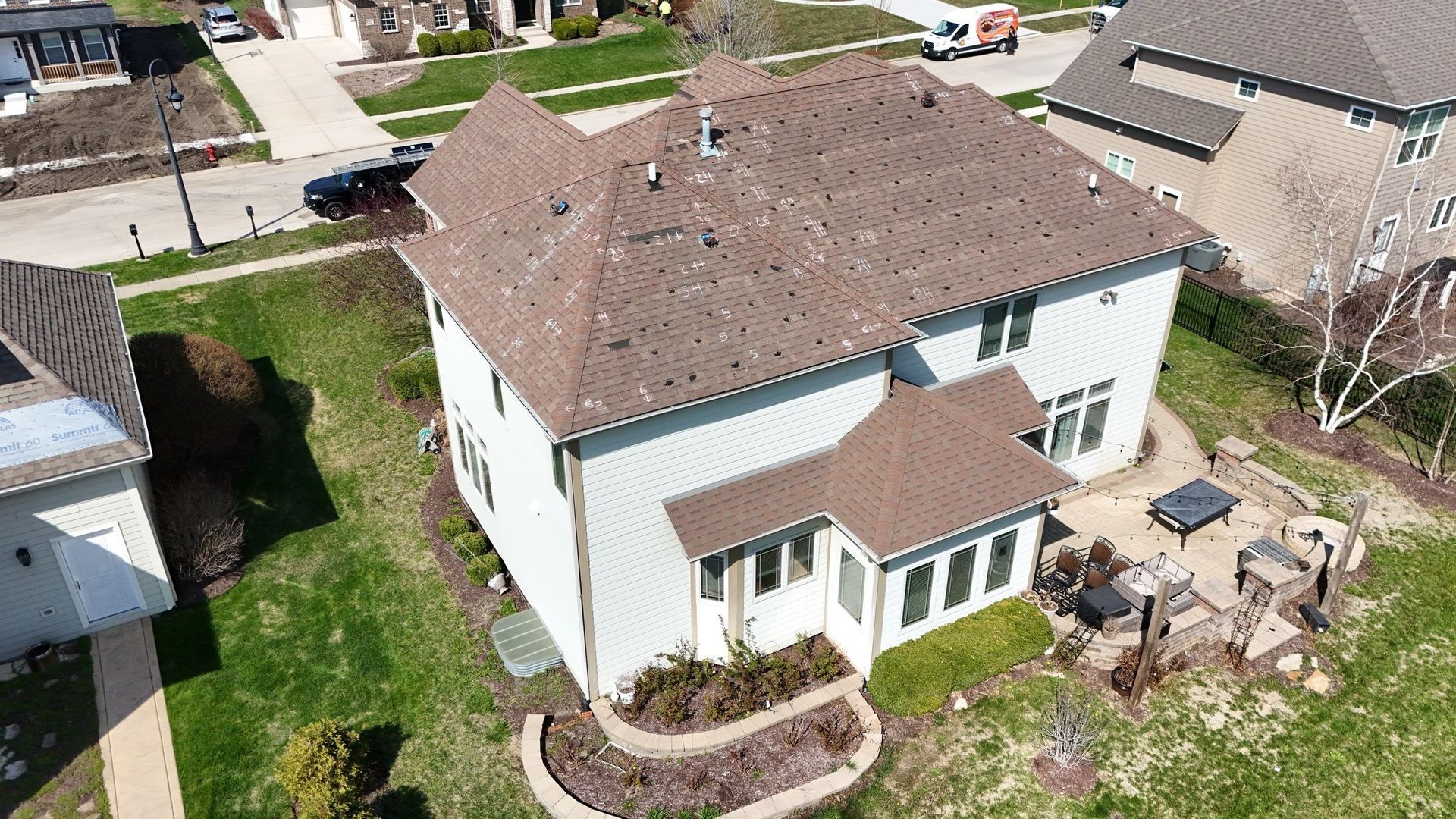 Two-story white house with brown roof, patio, and front landscaping. Green lawn surrounds.