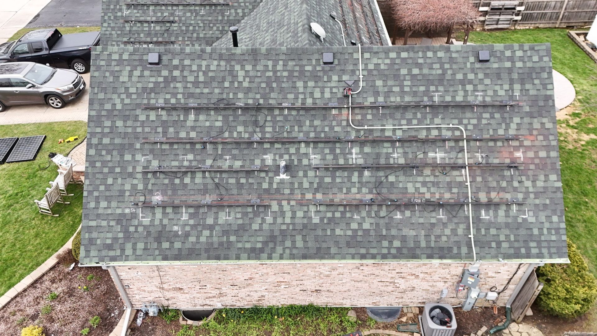 Overhead view of a house roof with worn, green shingles. Black lines cross the roof; vehicles and lawn visible.