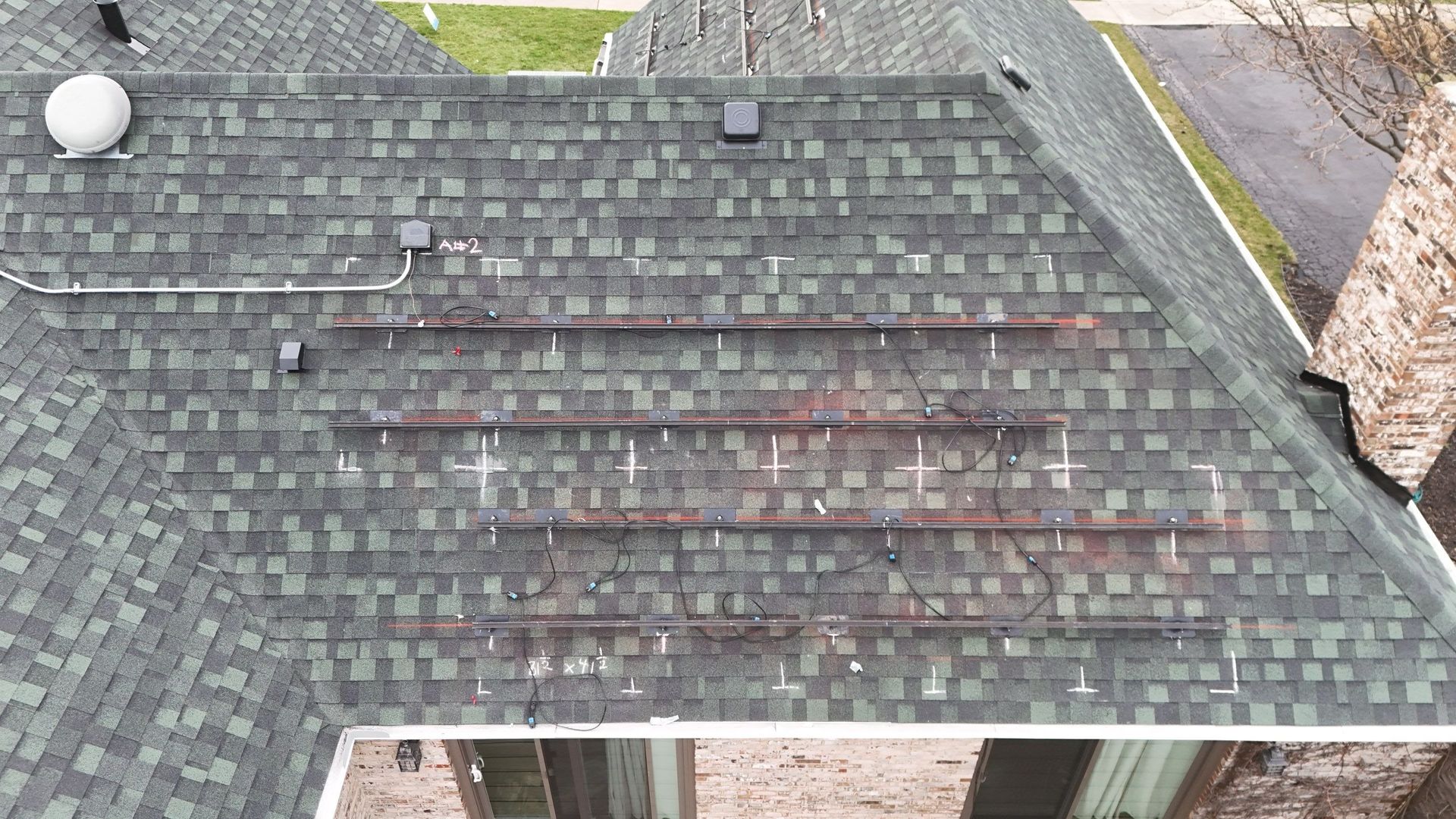 Overhead view of a dark green shingle roof with three brown, metal gutter sections.