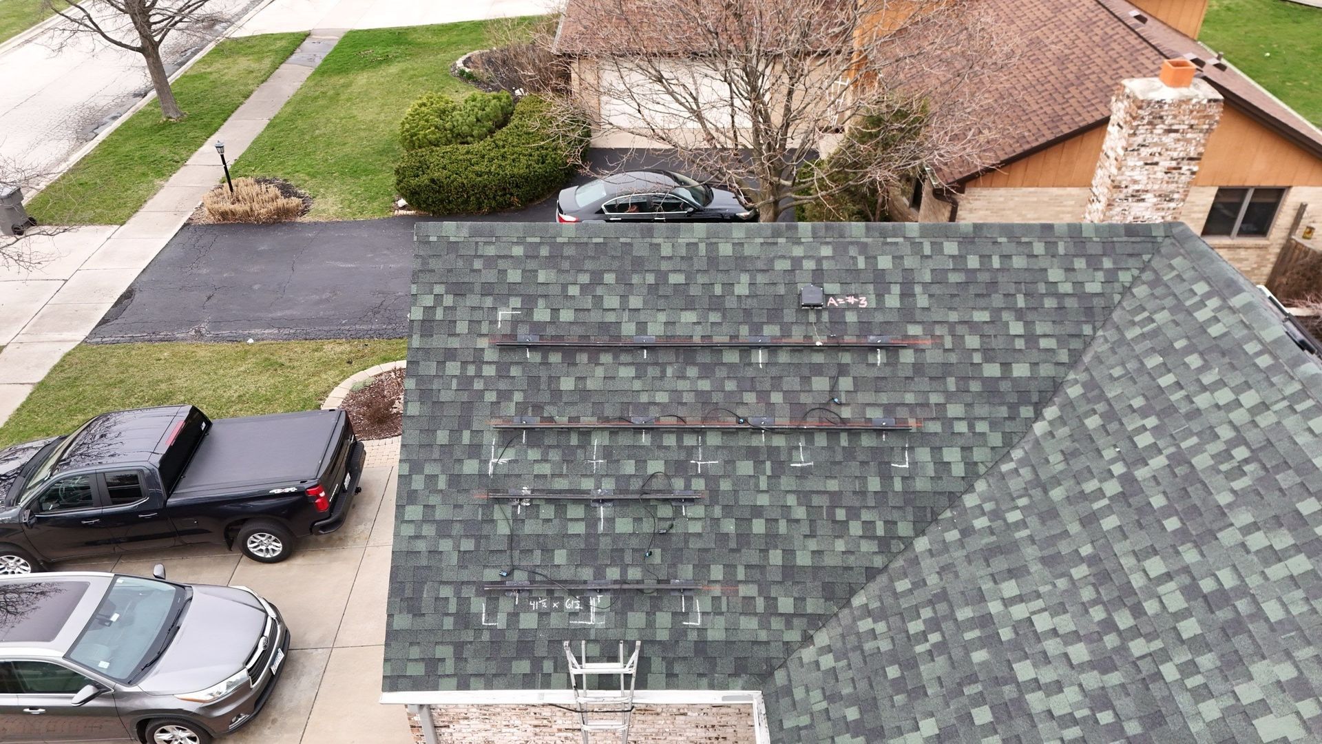Overhead view of house with dark green roof and parked vehicles.