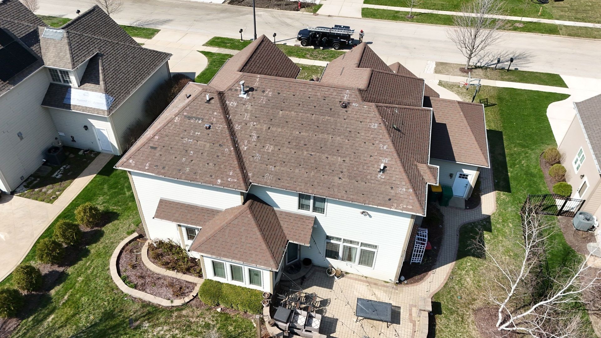 Aerial view of a two-story house with a brown roof and a paved patio surrounded by grass.