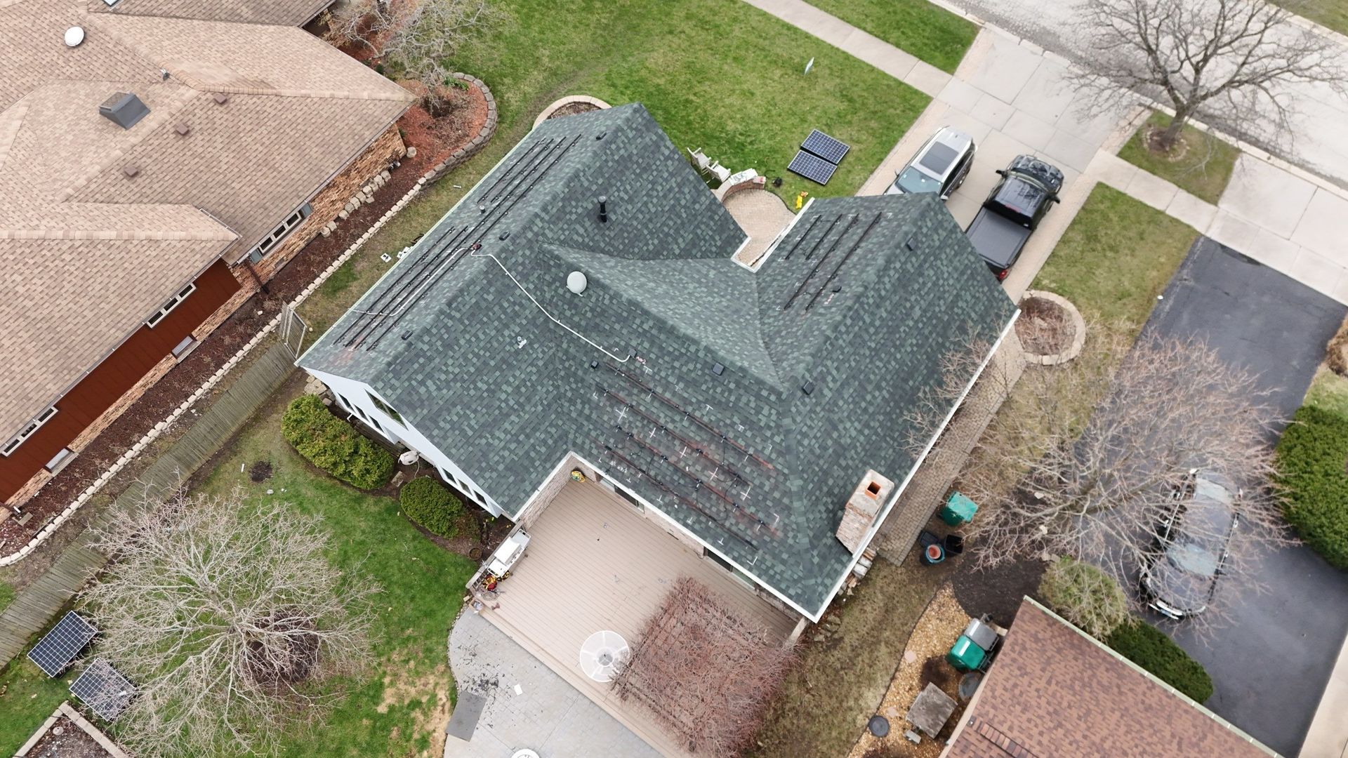Aerial view of a house with a green roof and brown trim, next to a driveway and green lawn.