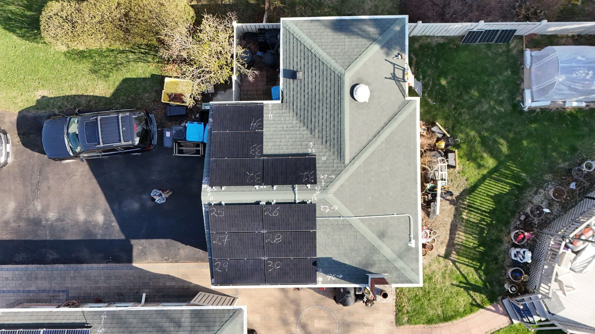 Aerial view of a house with solar panels on the roof; a car and yard are visible.