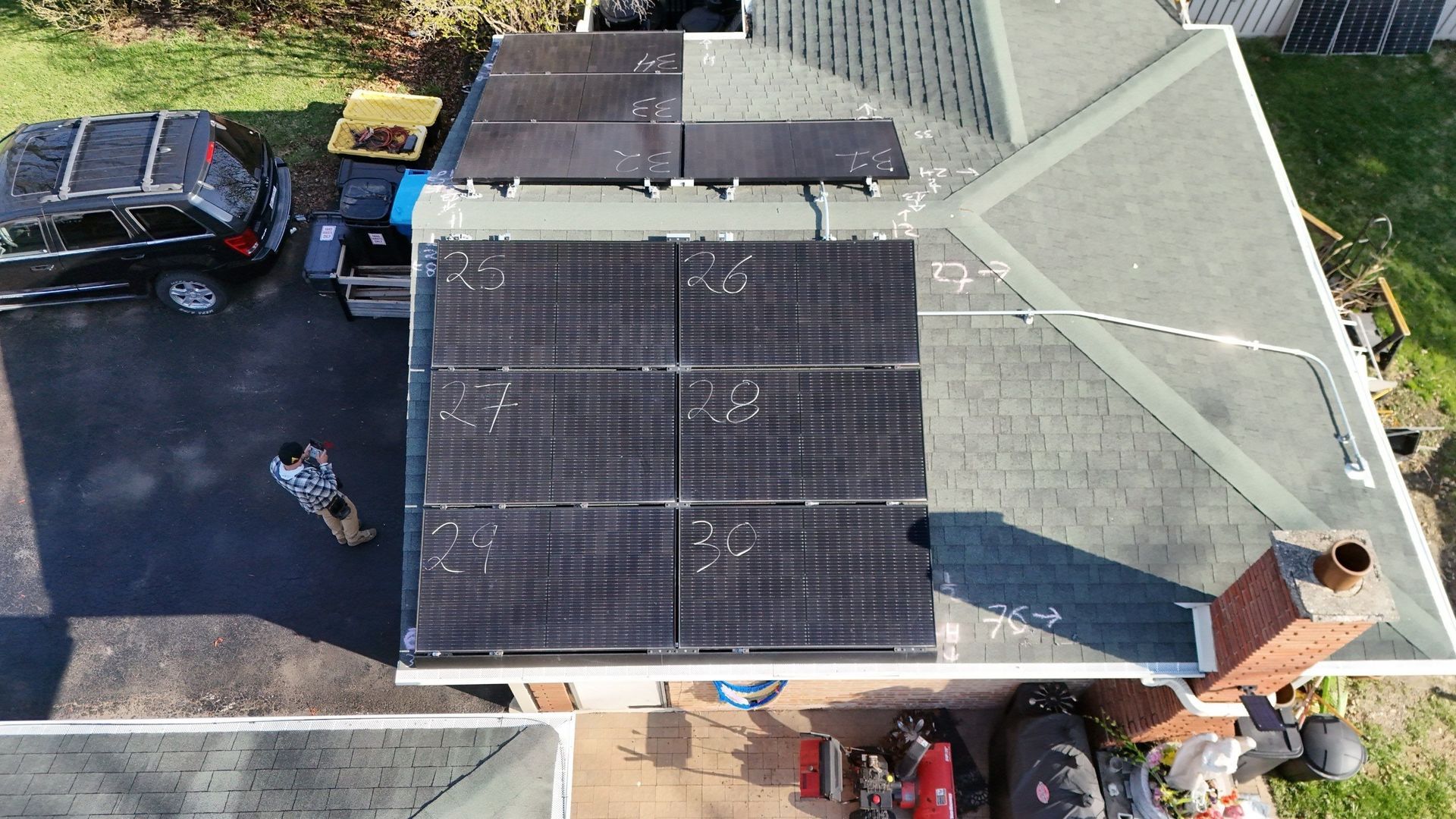 Overhead view of a house with solar panels on the roof, a black SUV, and a small dog.