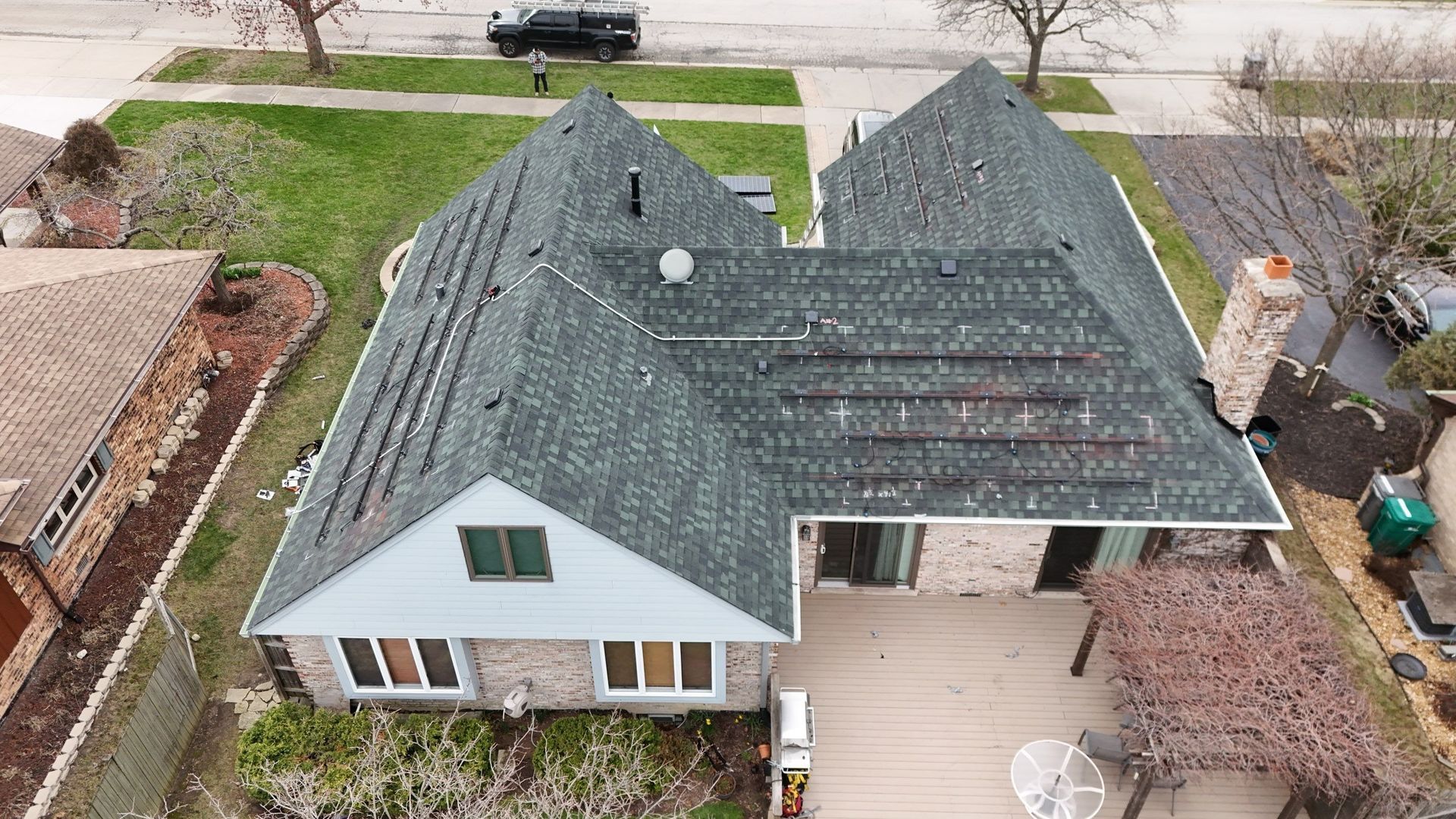 Aerial view of a house with a dark green roof, solar panels, and a wooden deck.