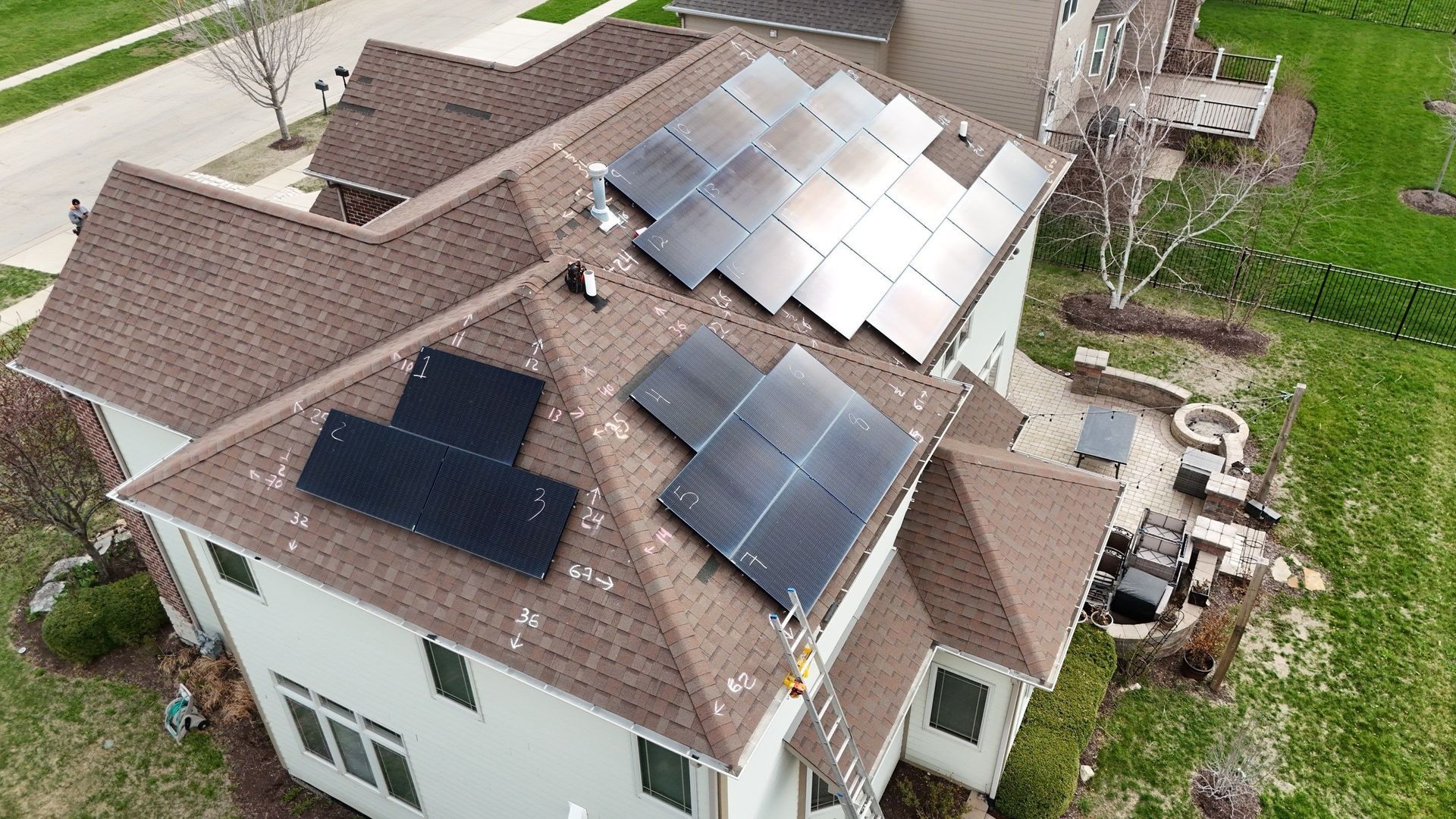 Solar panels on the brown roof of a two-story house with a lawn and nearby street.