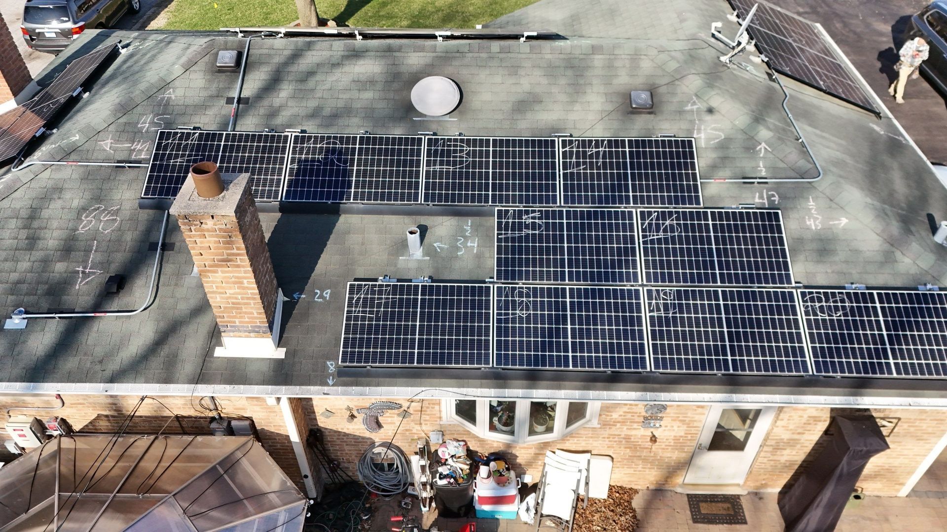 Overhead view of a house roof with solar panels, chimney, and visible windows.