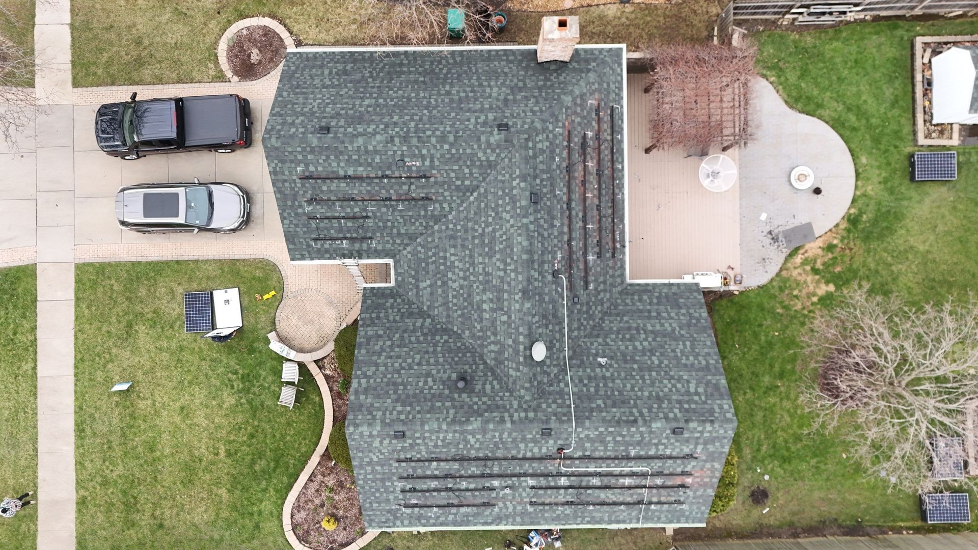 Overhead view of house with green roof, solar panels, driveway with two vehicles, and yard.