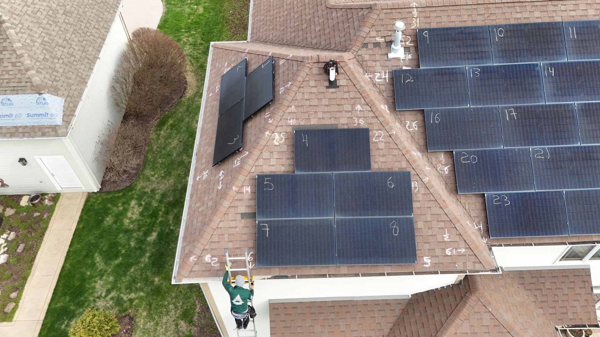 Solar panels being installed on a residential roof. A worker on a ladder is visible.