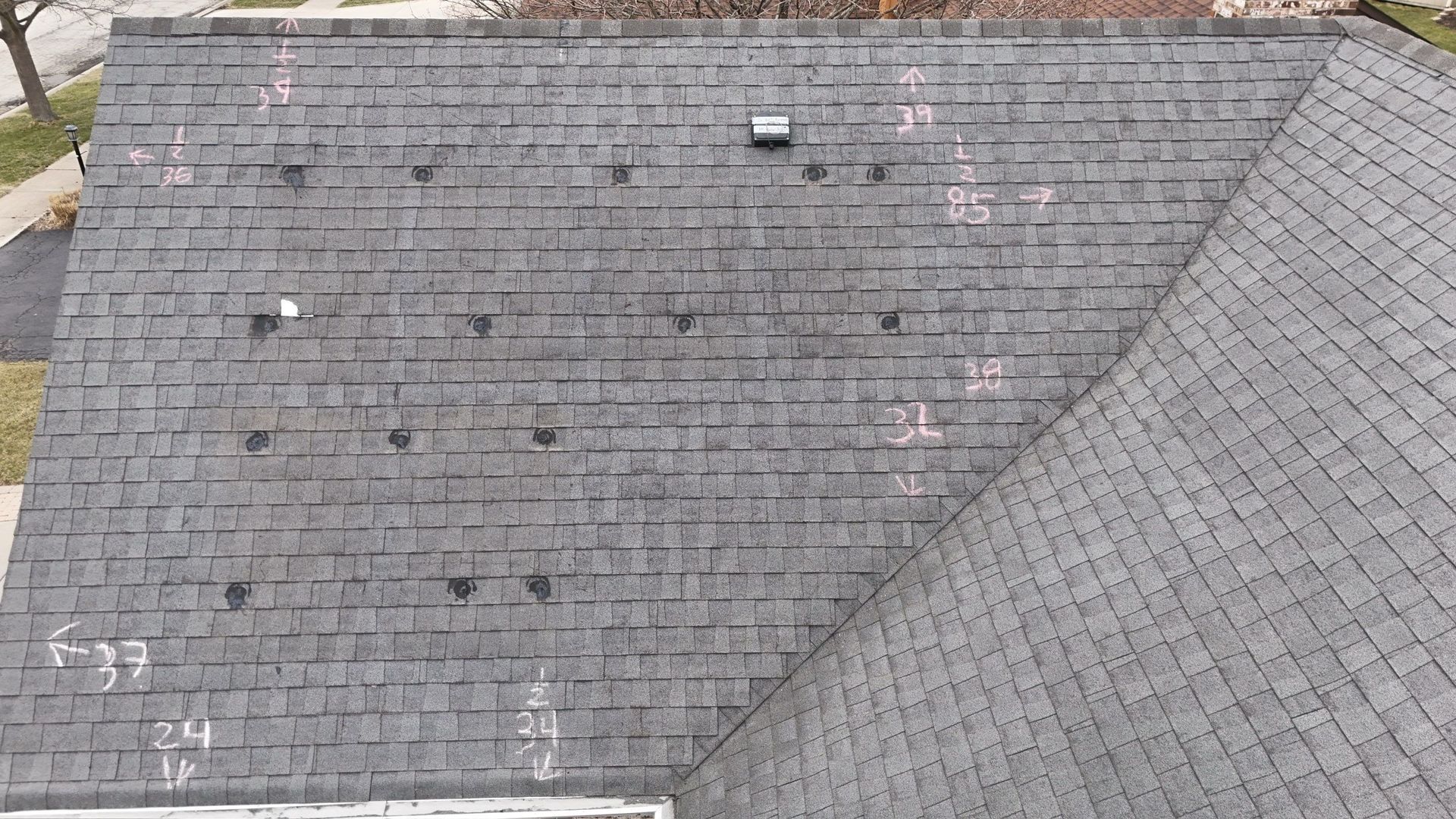 Overhead view of an aged asphalt shingle roof, with several visible holes marked with numbers.