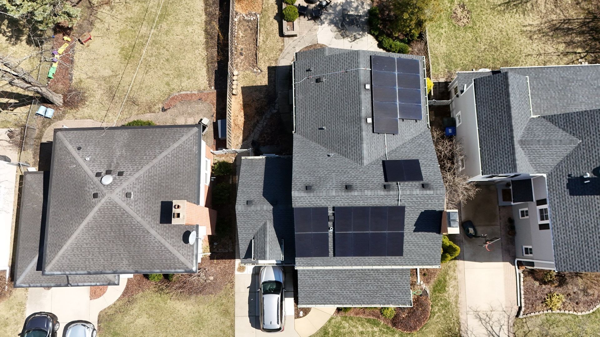 Overhead view of a house with solar panels on its roof. Other houses and a car are visible in a suburban setting.