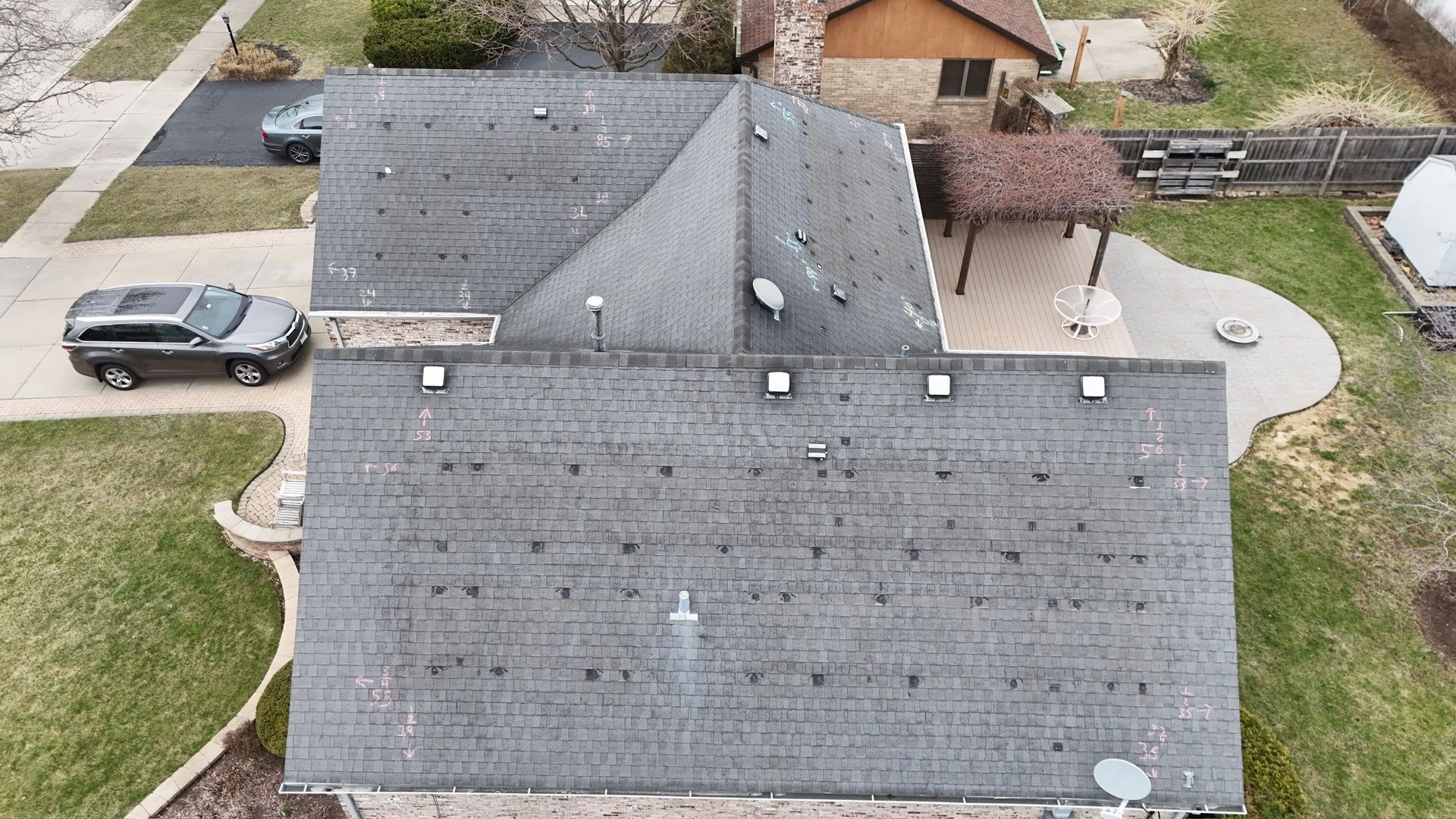 Overhead view of a house with dark grey shingles, a grey SUV in the driveway, and a patio with a seating area.