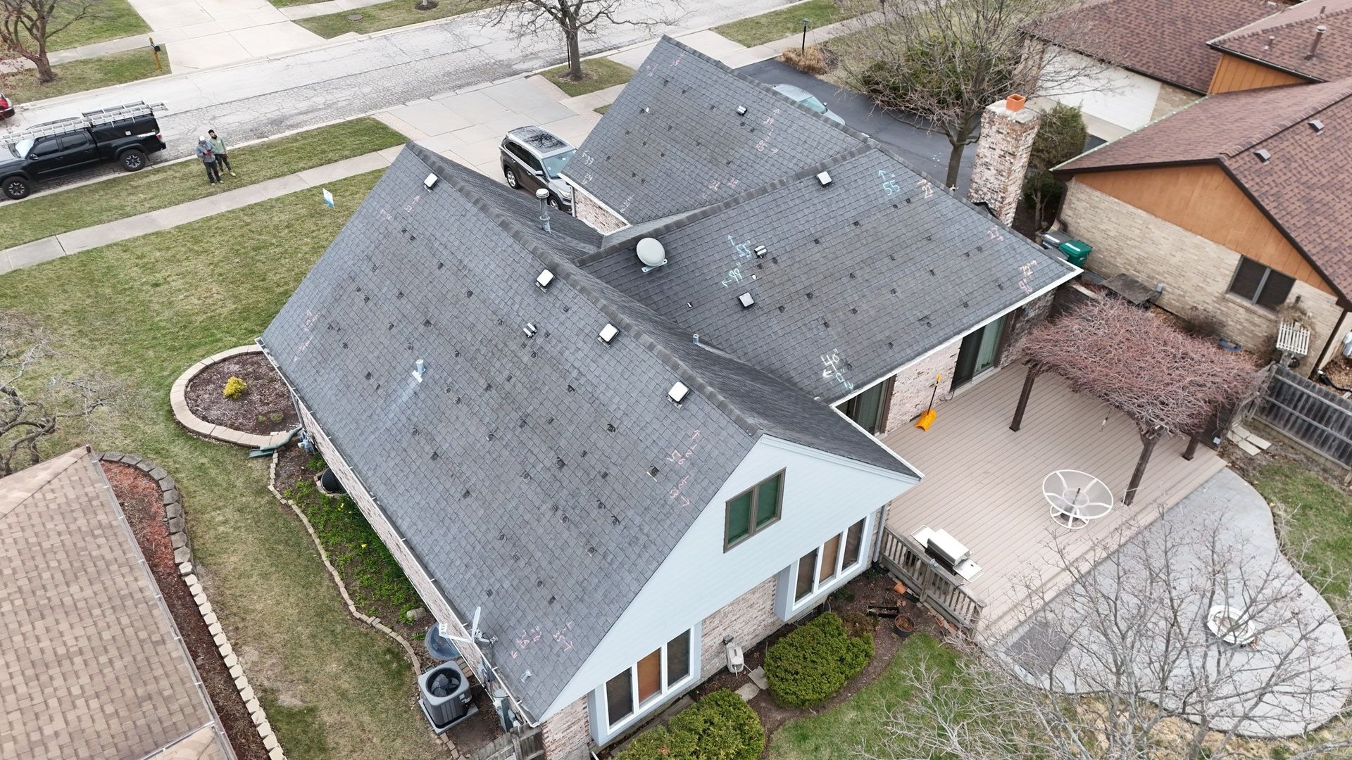 Overhead view of a suburban house with gray shingles, patio, and surrounding greenery.