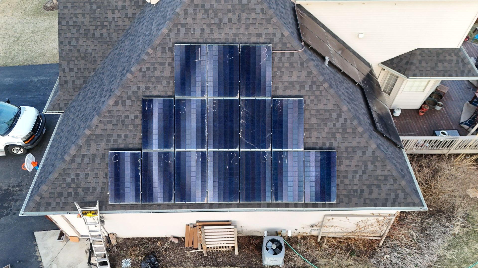 Solar panels installed on a residential roof, with a white van and air conditioning unit visible.
