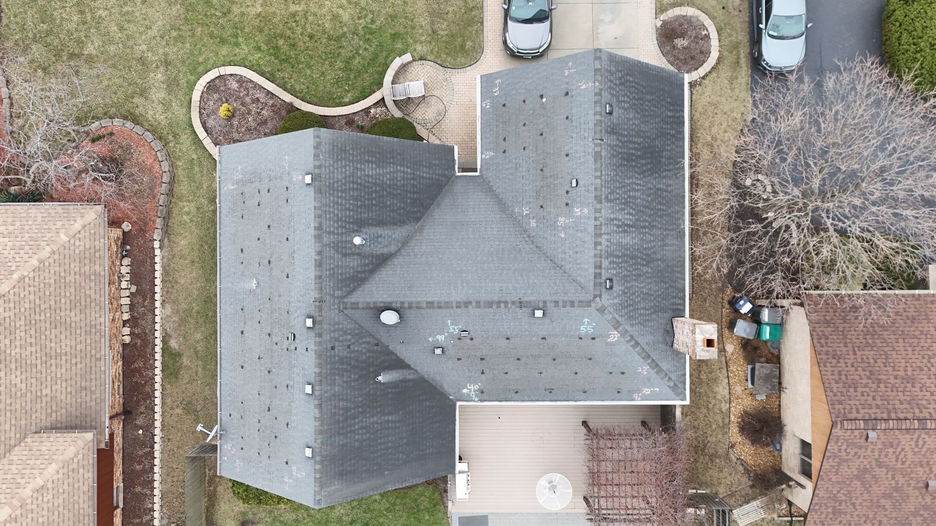 Overhead view of a house with a gray roof and a driveway, surrounded by lawns and other houses.