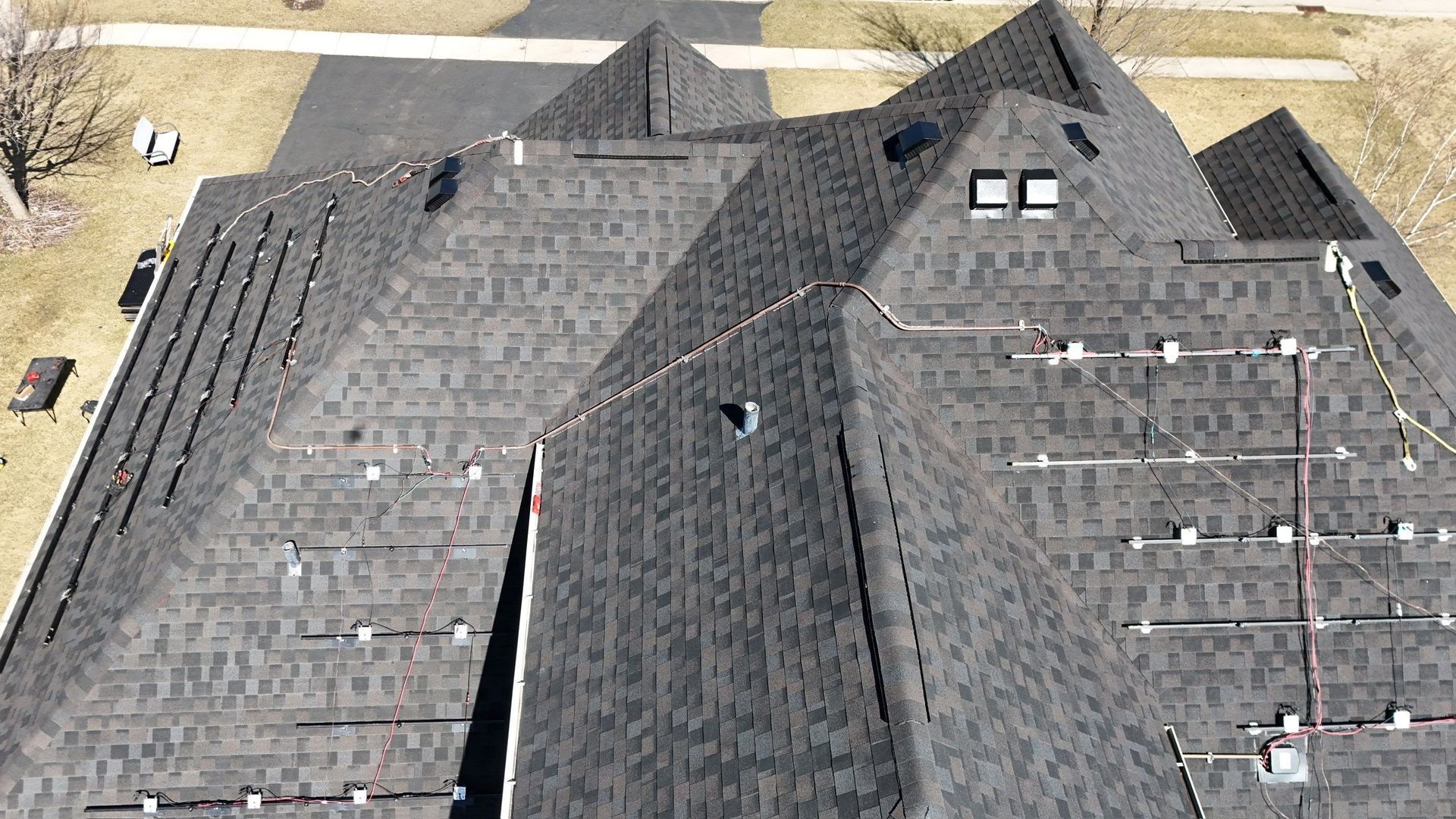 Overhead view of a dark shingle roof with multiple peaks and solar panels.