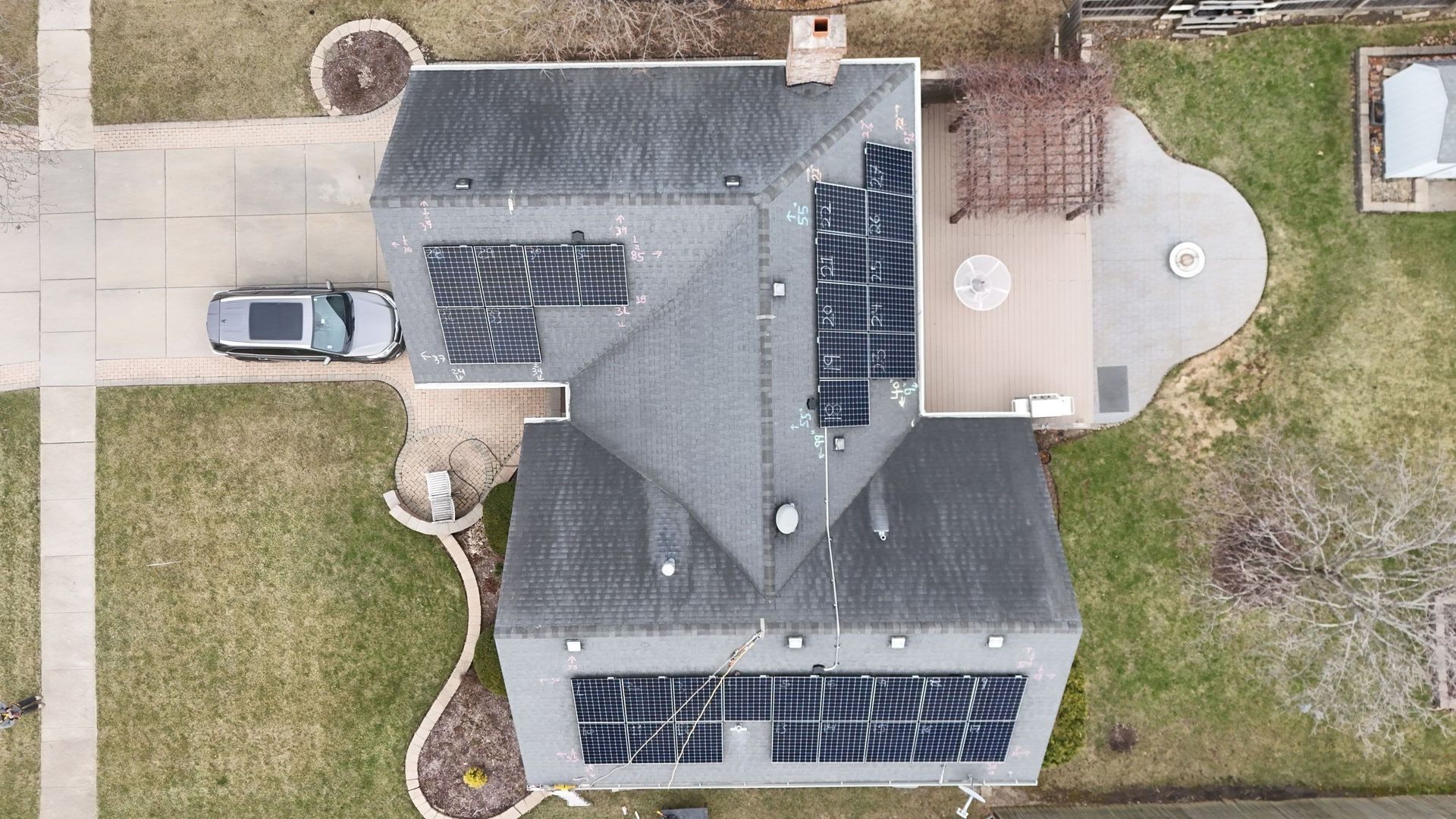 Aerial view of a house with solar panels on the roof, a car in the driveway, and a patio.