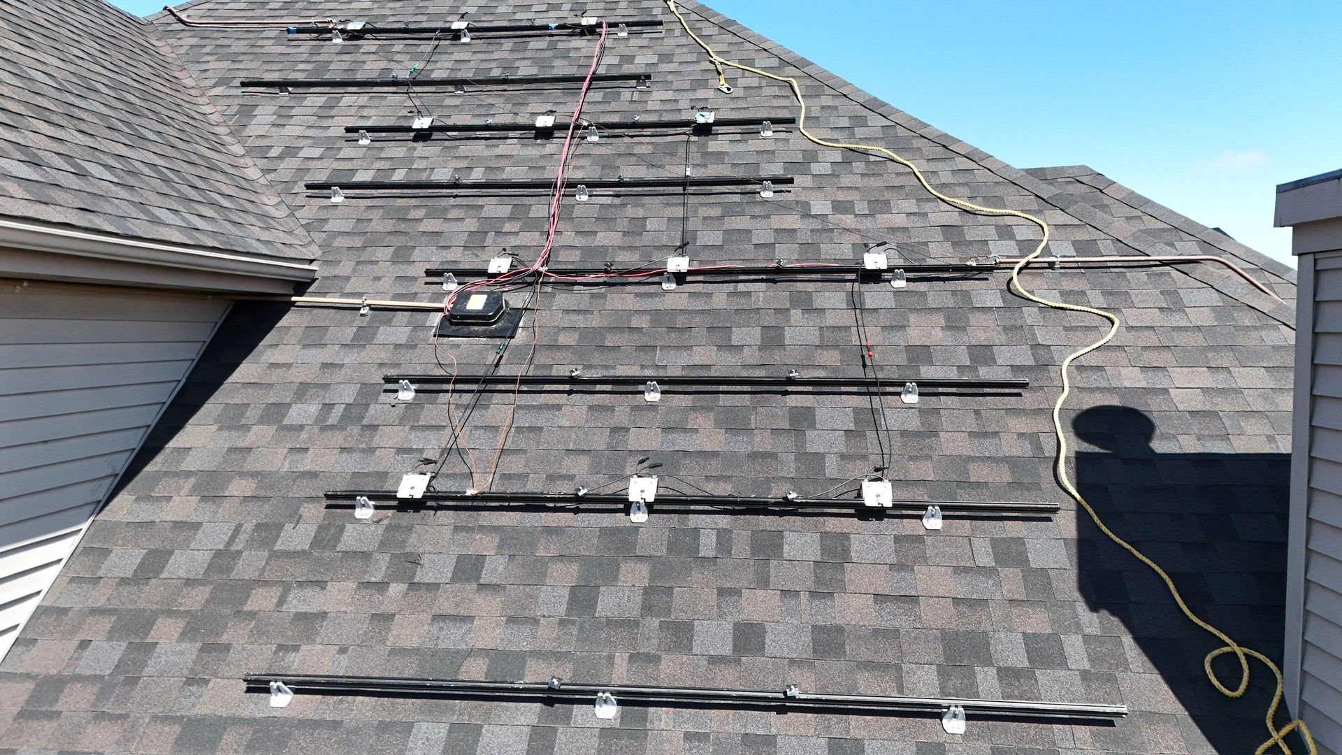 Solar panel mounting system on a shingle roof, with black rails and wiring.
