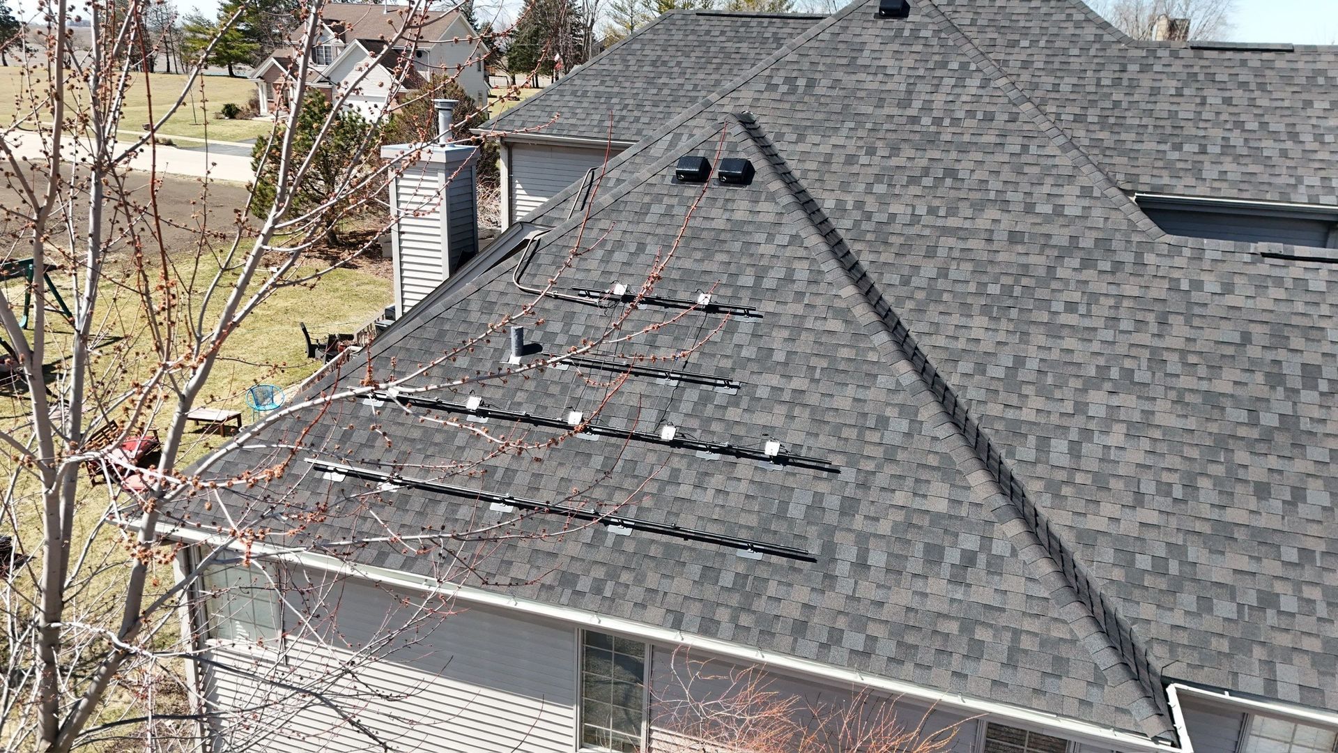 A house with a dark gray shingled roof; vents and gaps are visible, possible roof damage.