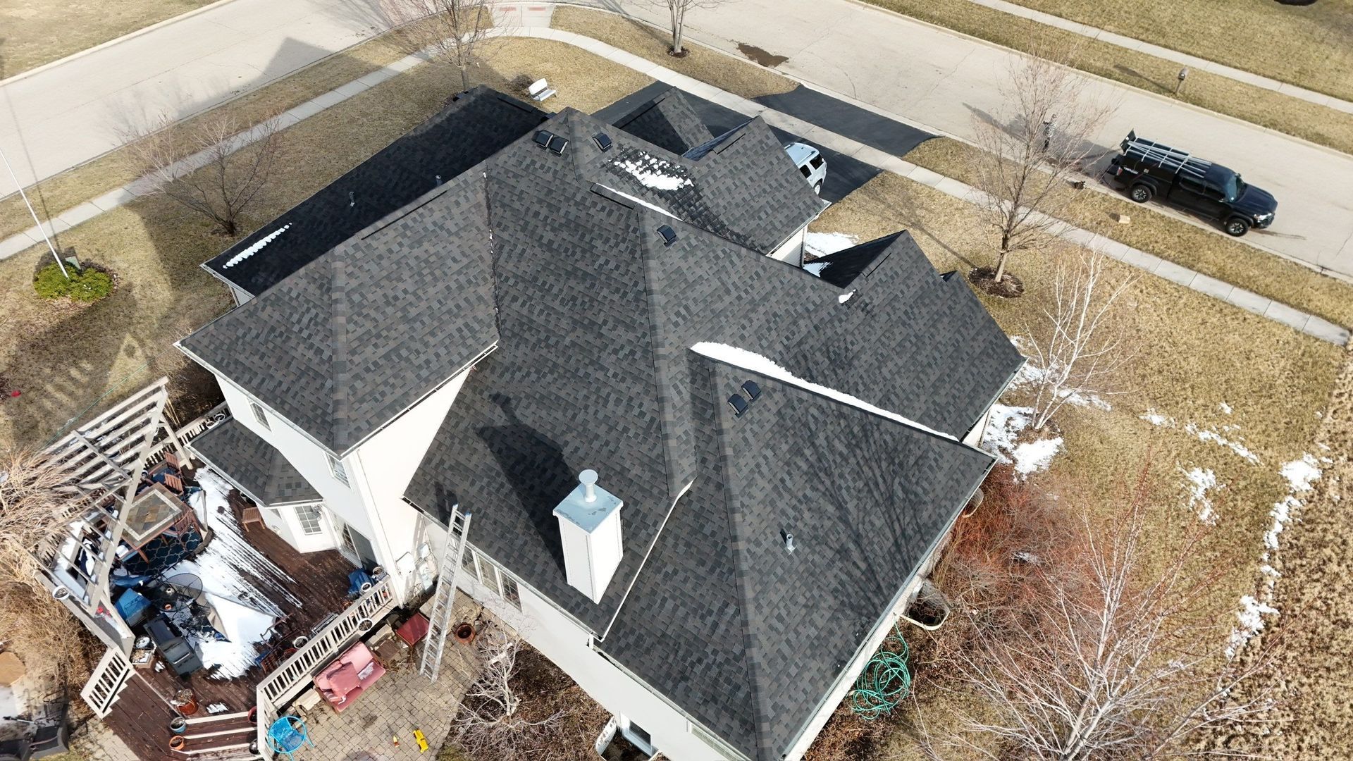 Overhead view of a house with a dark gray roof, a backyard deck, and a street in winter.