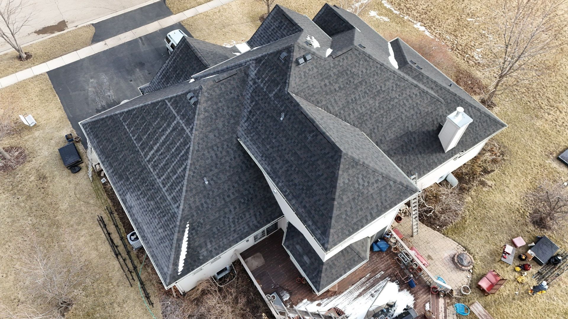 Overhead view of a house with a dark roof, a driveway, and surrounding brown grass.