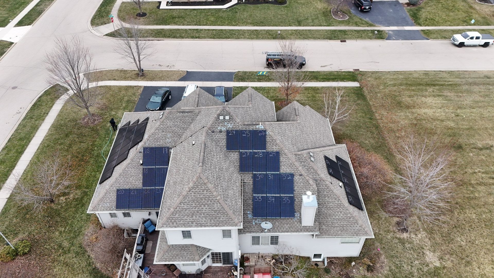 Overhead view of a house with solar panels on the roof, a car parked in the driveway, and a suburban street.