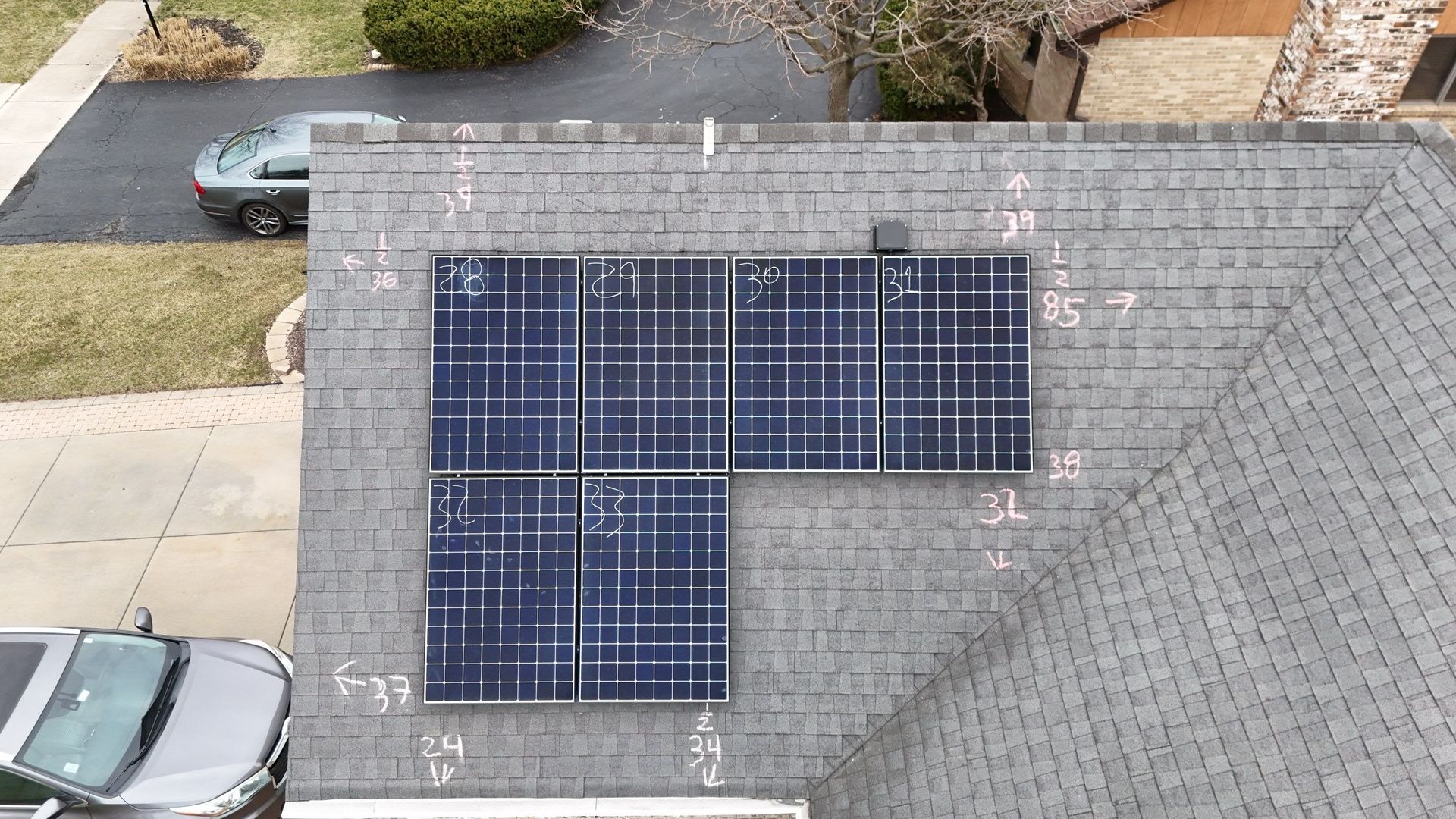 Aerial view of a residential roof with solar panels installed. Car and driveway are visible.
