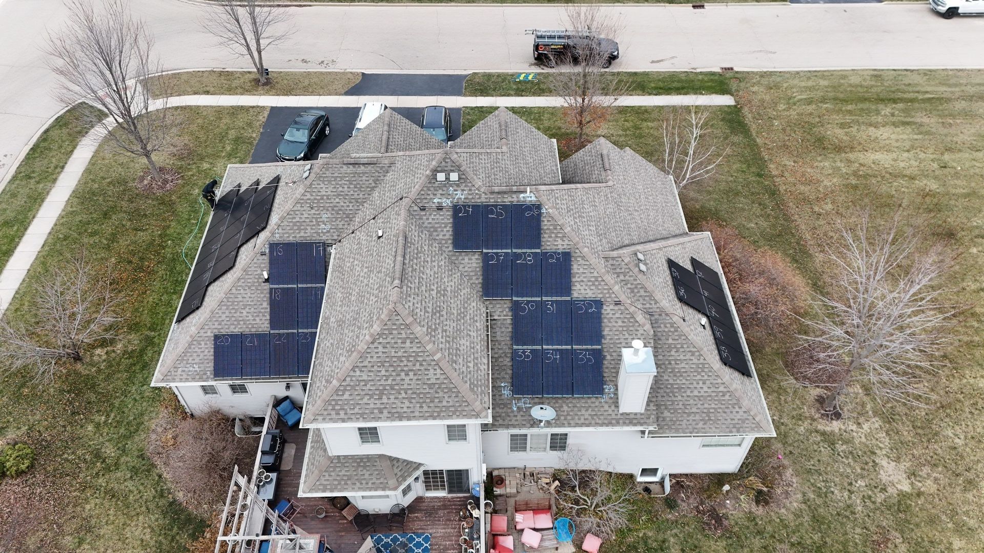 Overhead view of a house with solar panels on the roof, a car in the driveway, and surrounding trees and grass.