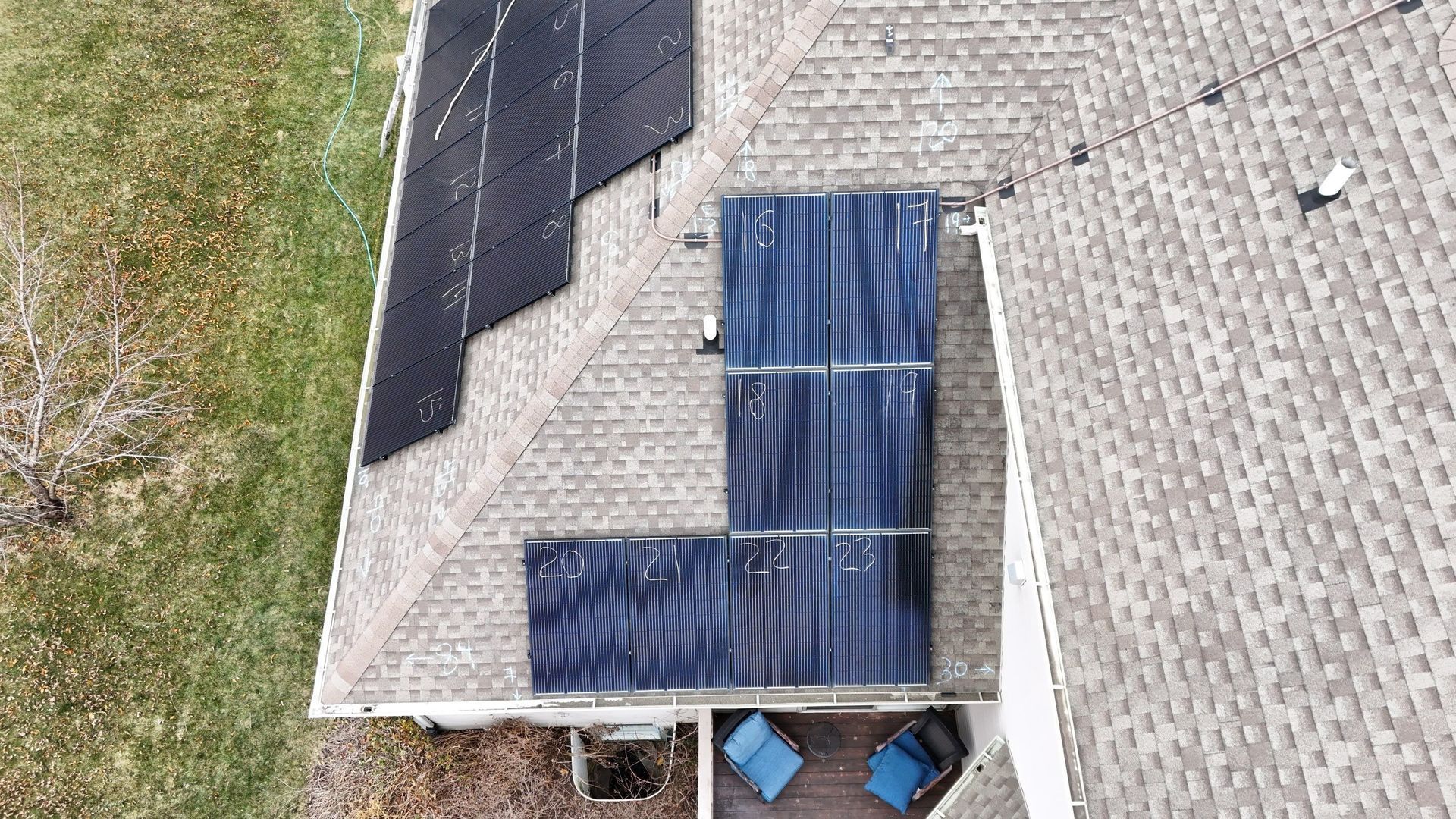 Overhead view of a roof with solar panels. A deck with blue chairs is beneath the roof.