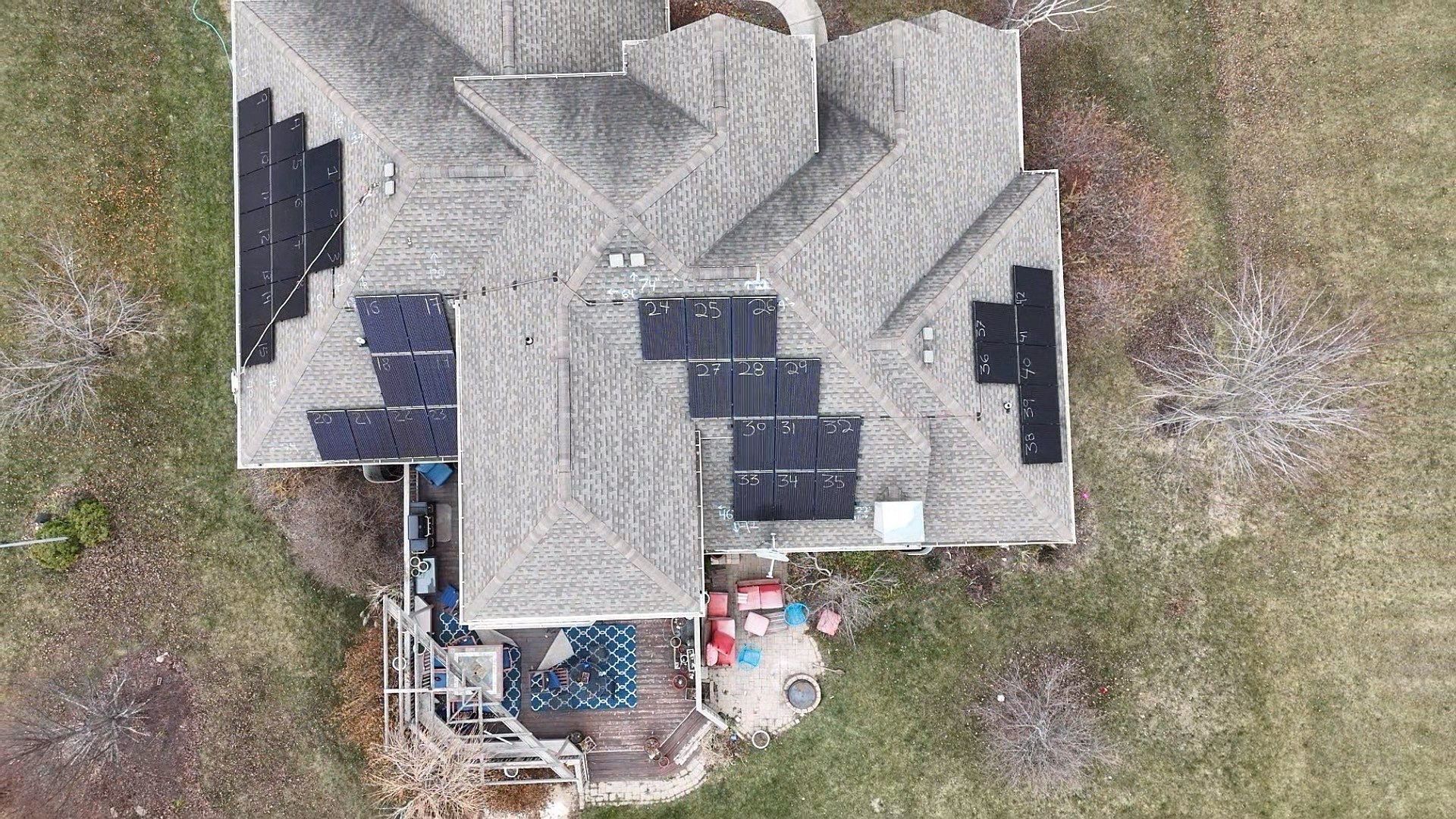 Overhead view of a house with solar panels on the roof, surrounded by grass and a deck.