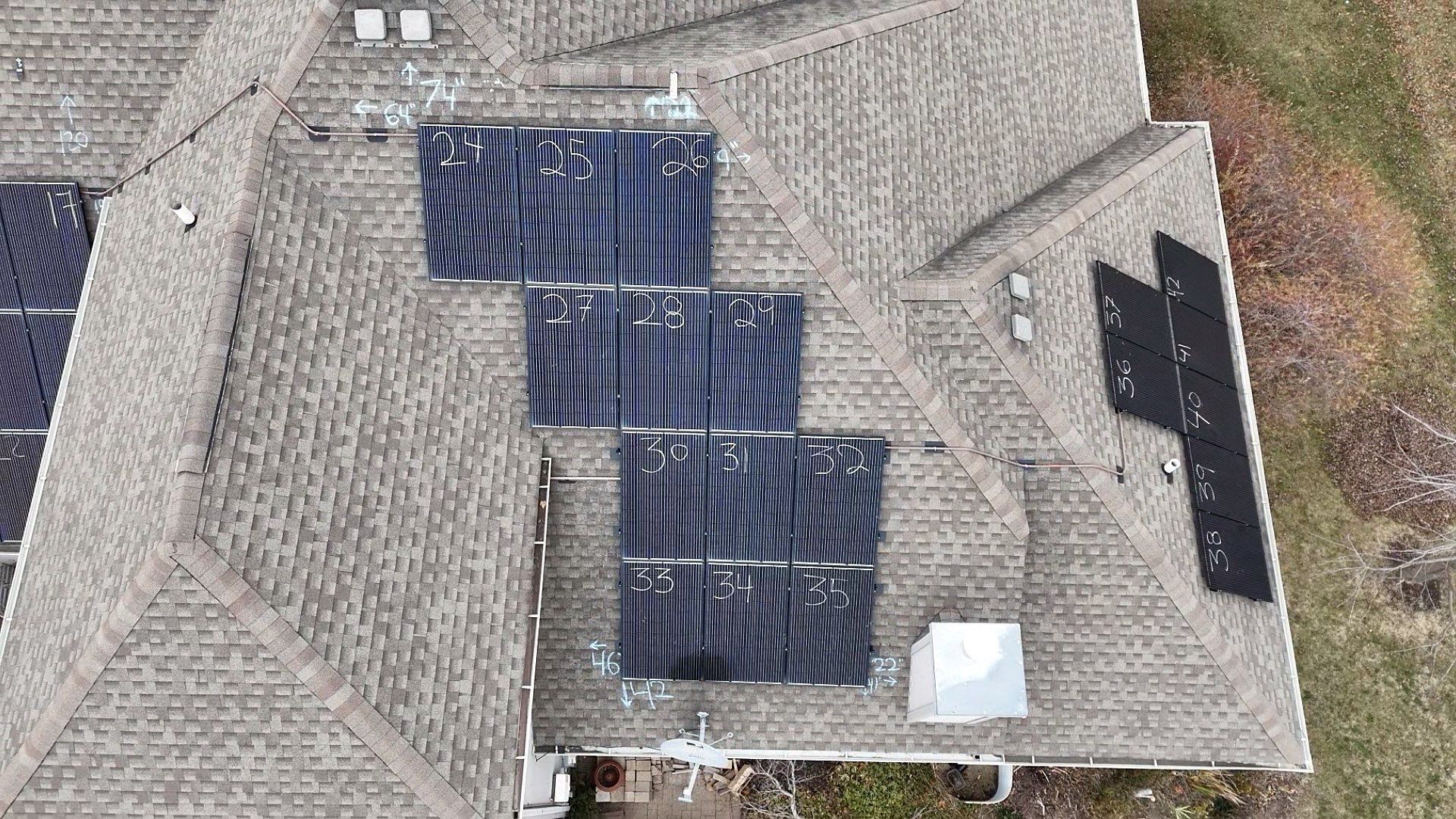 Aerial view of a house roof with solar panels installed, gray shingles, and a white vent.