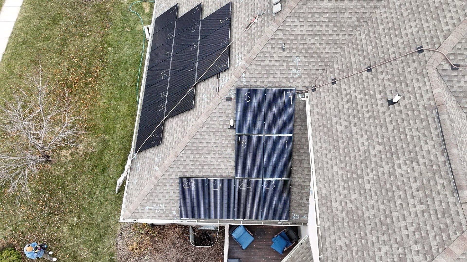 Overhead view of solar panels on a roof, with a grassy lawn and chairs below.