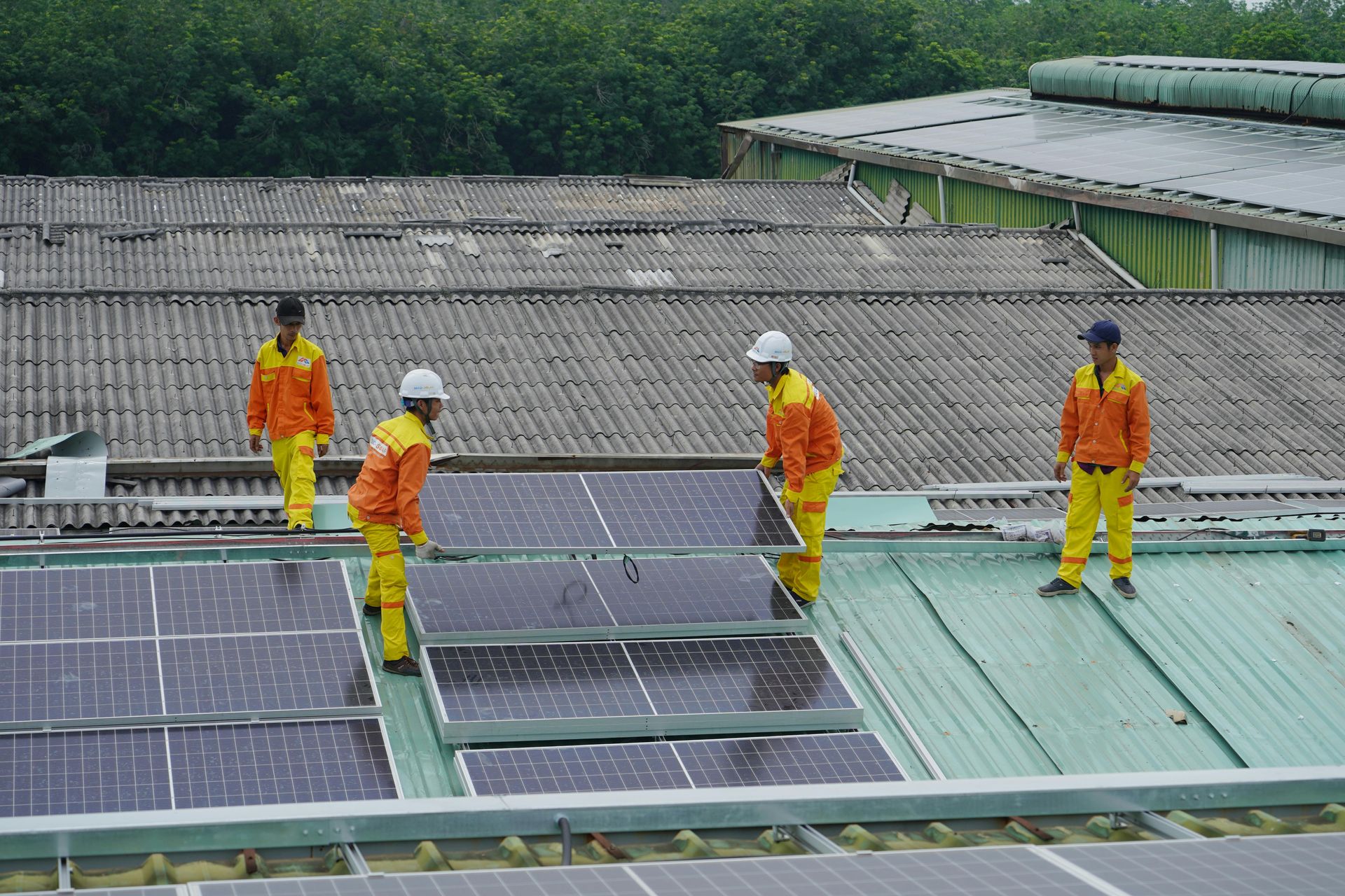 Four workers in orange uniforms installing solar panels on a rooftop.