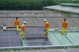 Four workers in orange uniforms installing solar panels on a rooftop.