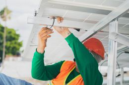 Person in orange vest and helmet installing solar panels.