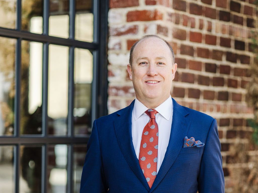 Adam P. Plant in a suit and tie is standing in front of a brick building.