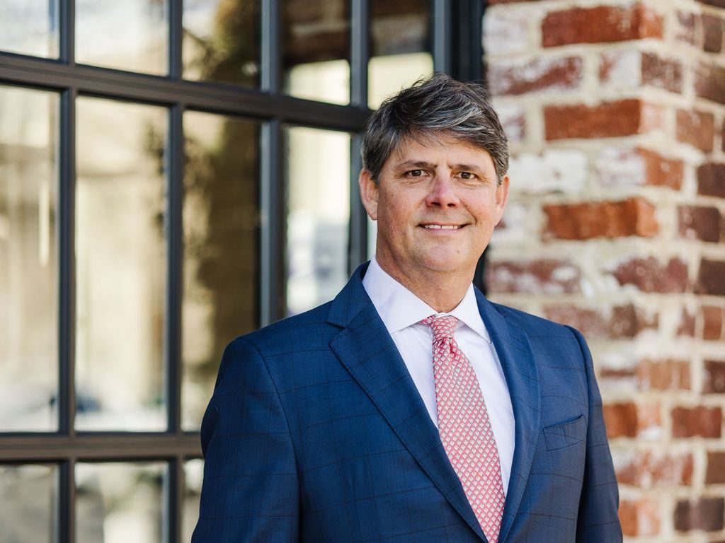 Harlan F. Winn, III wearing a suit and tie  standing in front of a brick building.