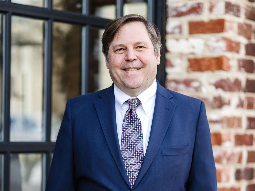 Robert E. Battle in a suit and tie is standing in front of a brick building.