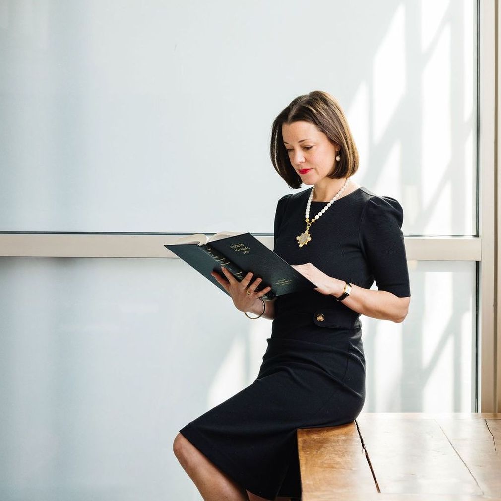 Mallory S. Morgan in a black dress is sitting on a table reading a book.