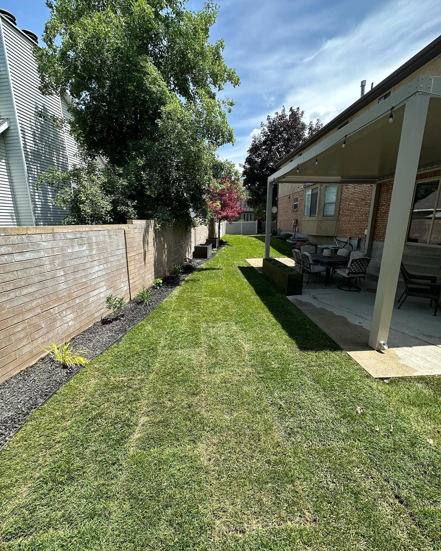 A backyard with a covered patio and a lush green lawn.