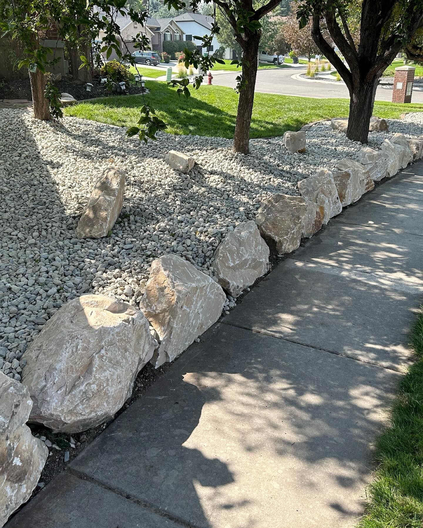 A sidewalk lined with rocks and gravel next to a yard.