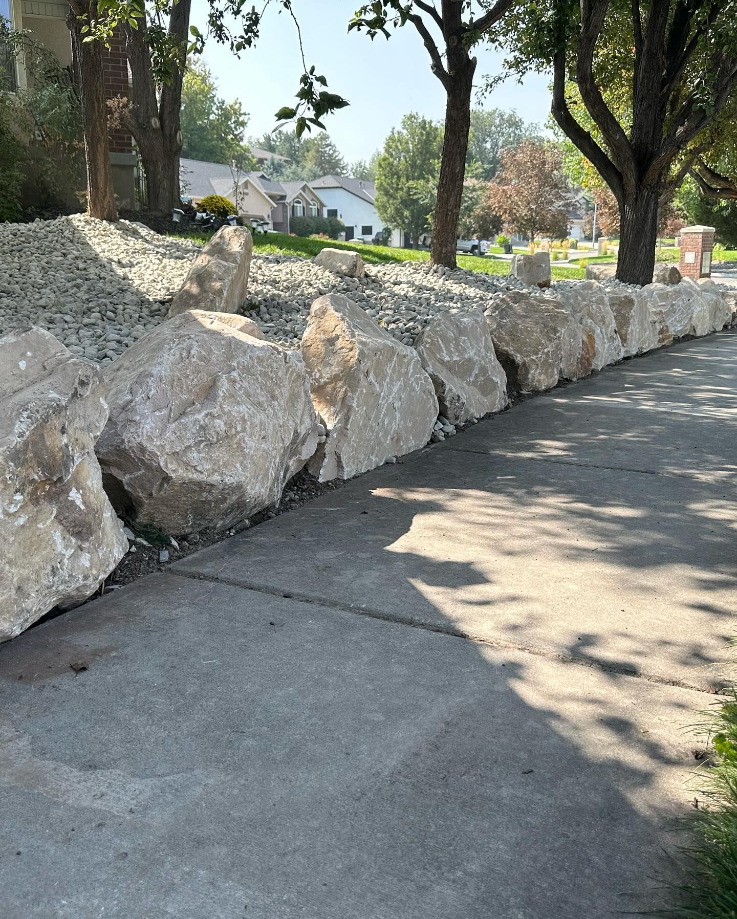 A stone wall along a sidewalk with trees in the background