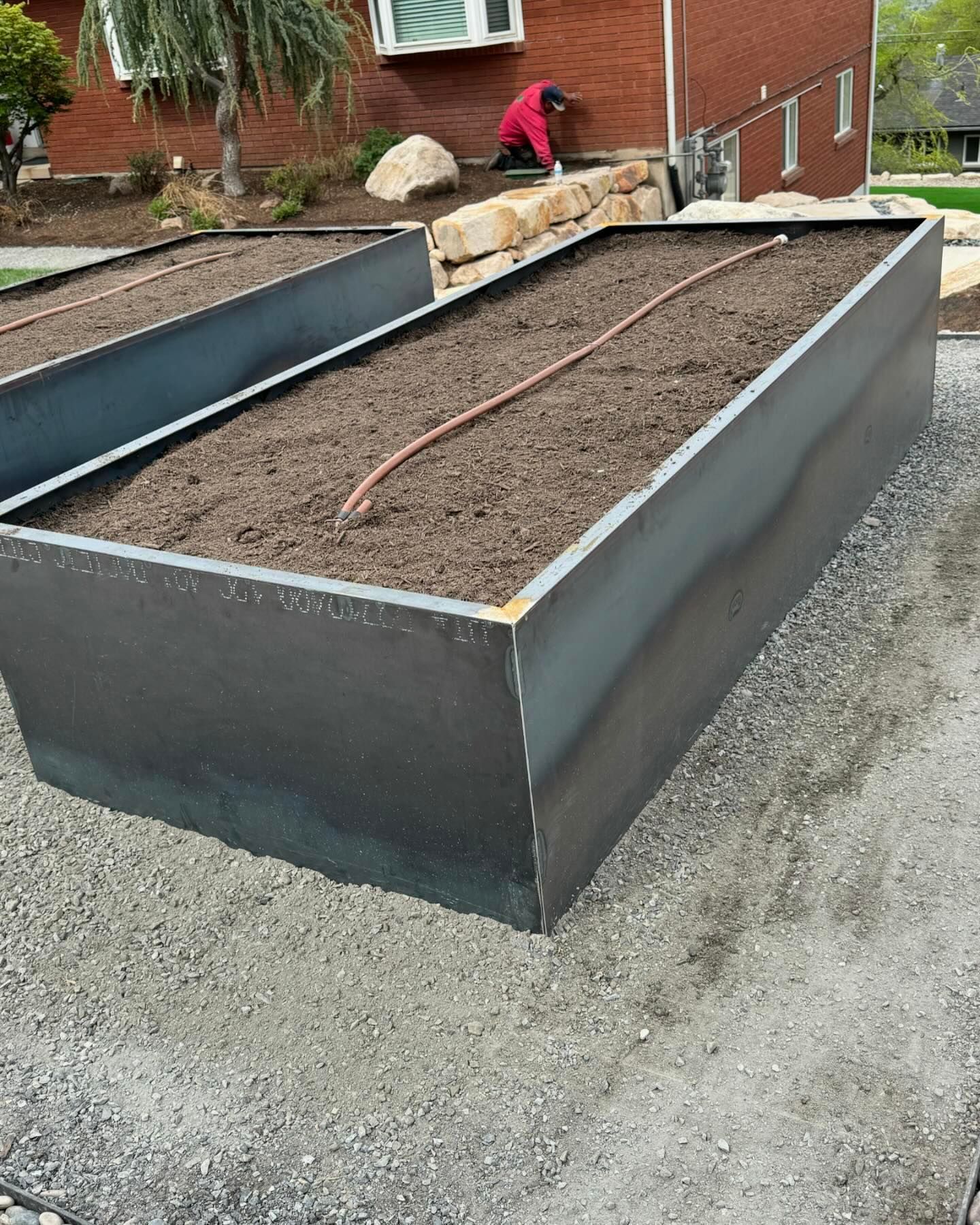 A man is working on a garden bed in front of a brick house.